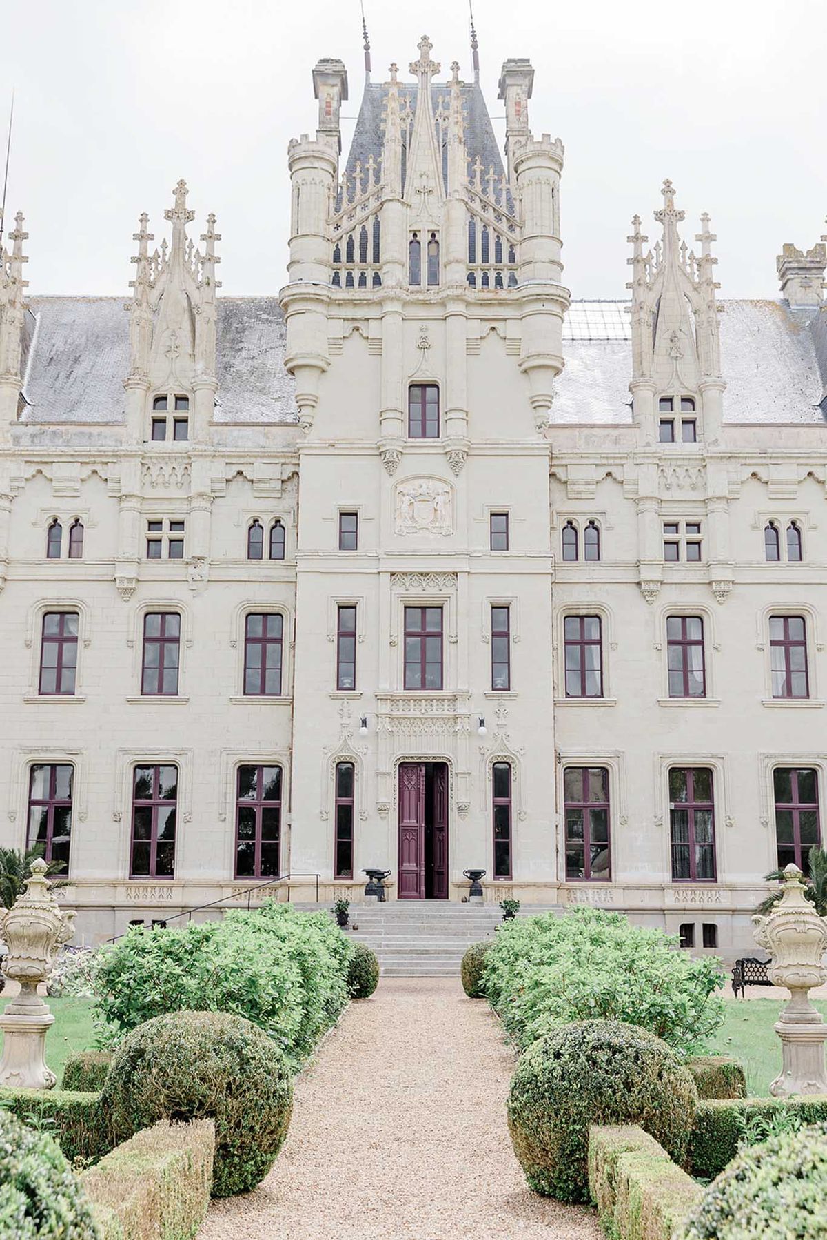 Neo-Gothic chateau with pointed spires, burgundy windows, and formal boxwood parterre garden