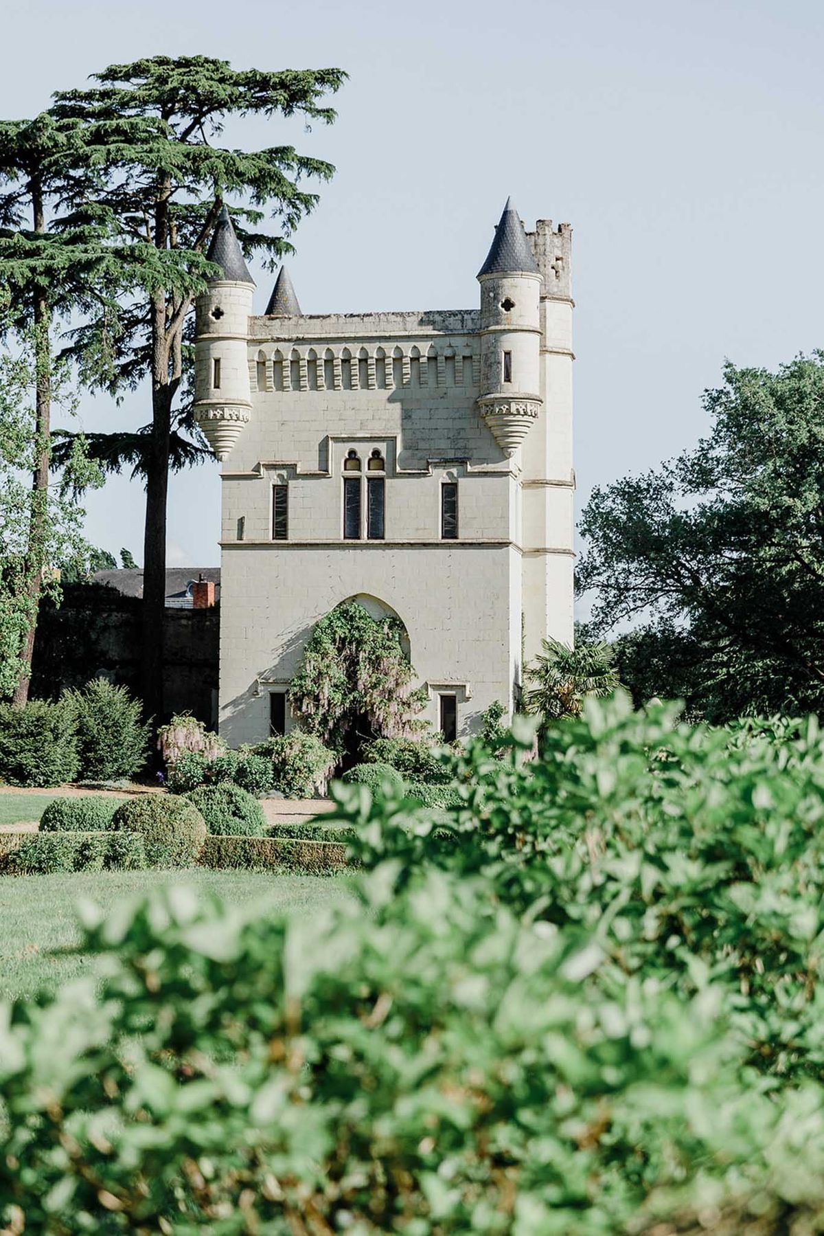 Chateau gatehouse with four turrets and wisteria-draped arched entrance surrounded by topiary