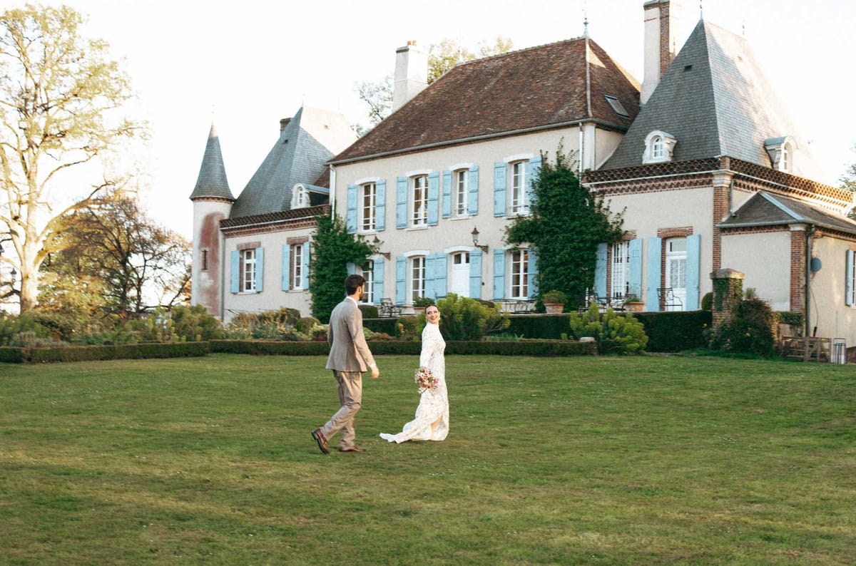 Bride and groom posing together on manicured lawn in front of French château-style manor