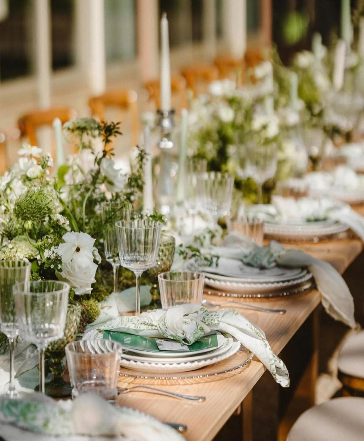 Farm table with gold chargers, botanical napkins, white ranunculus runner, and sage taper candles