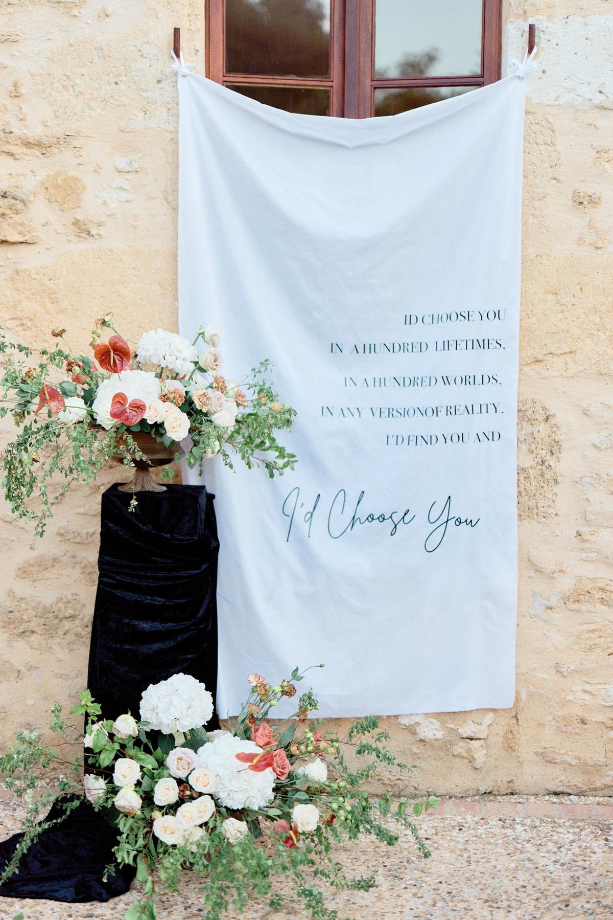 Quote banner with rust anthuriums, ivory roses, and blush ranunculus on black velvet pedestal