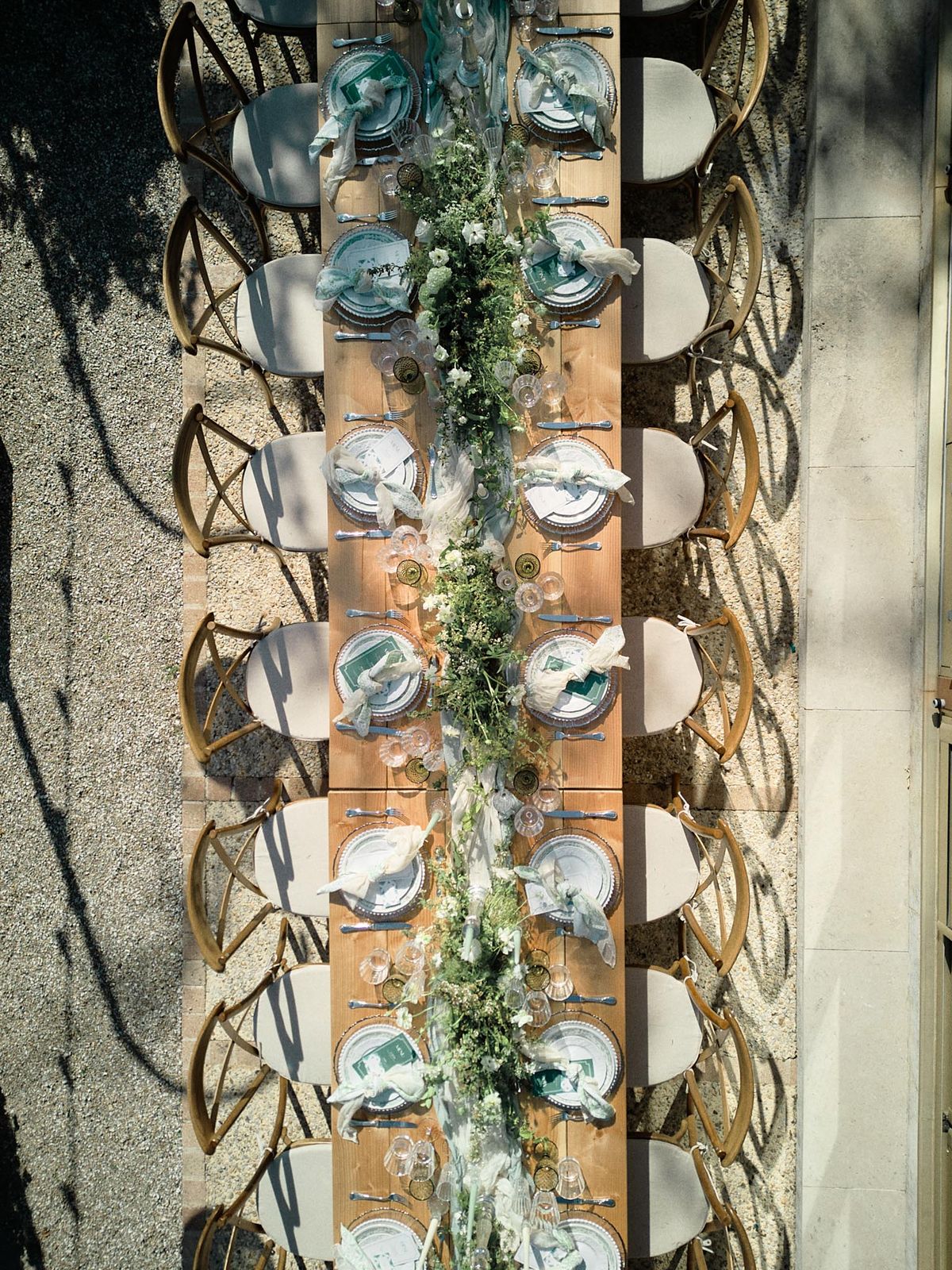 Aerial view of farm table with greenery runner, teal charger plates, and gold cross-back chairs