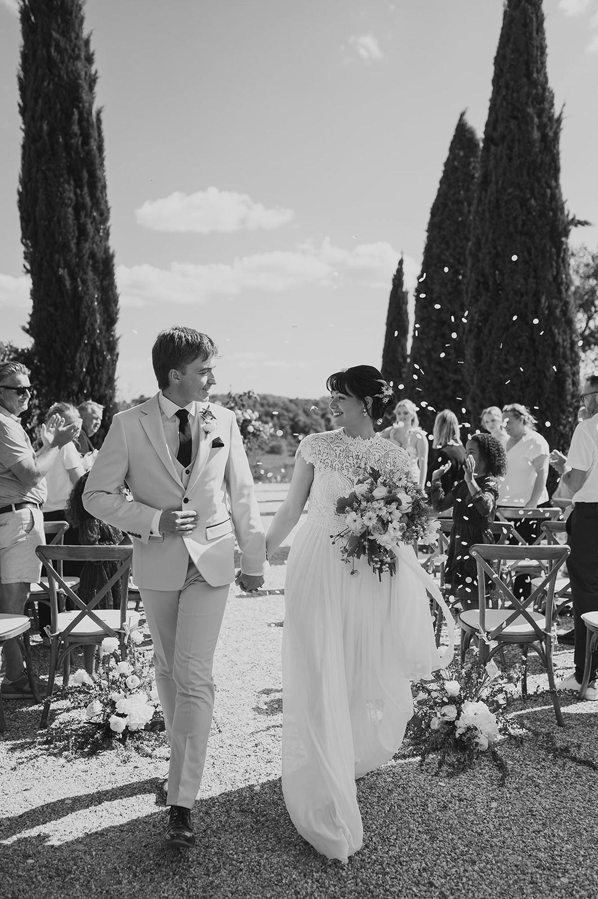 Black and white photo of bride and groom walking down the aisle as guests throw confetti after outdoor ceremony