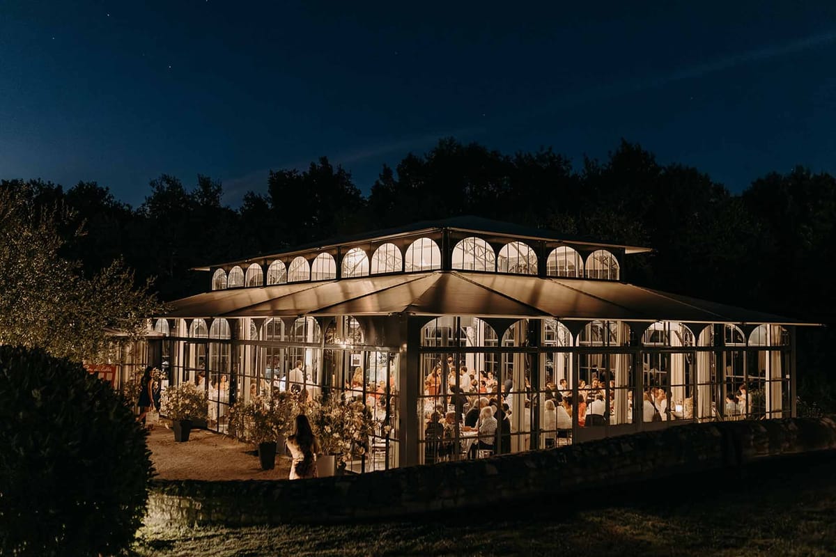 Glass orangery wedding reception lit up at night at Domaine de la Fauconnie