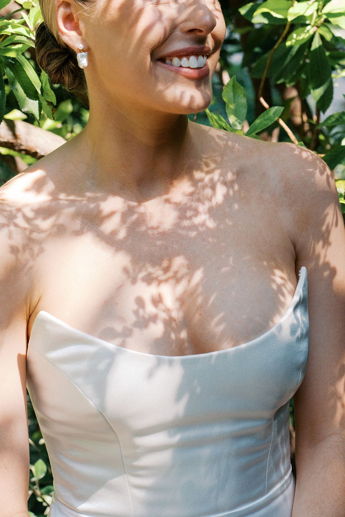 Bride smiling in dappled garden light wearing a strapless ivory gown at Restaurant l'Ile, Paris