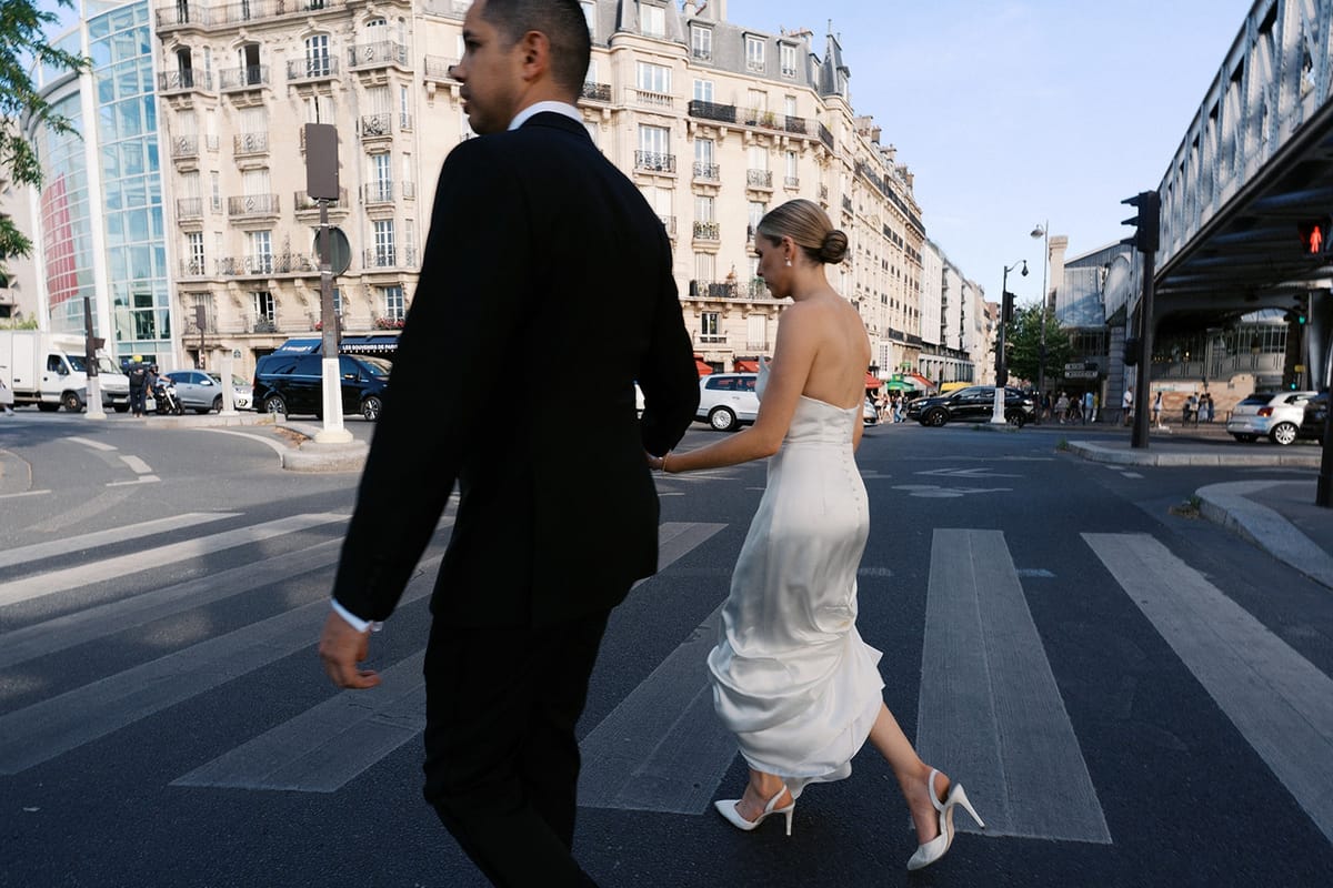 Couple holding hands across a Paris pedestrian crossing in summer light