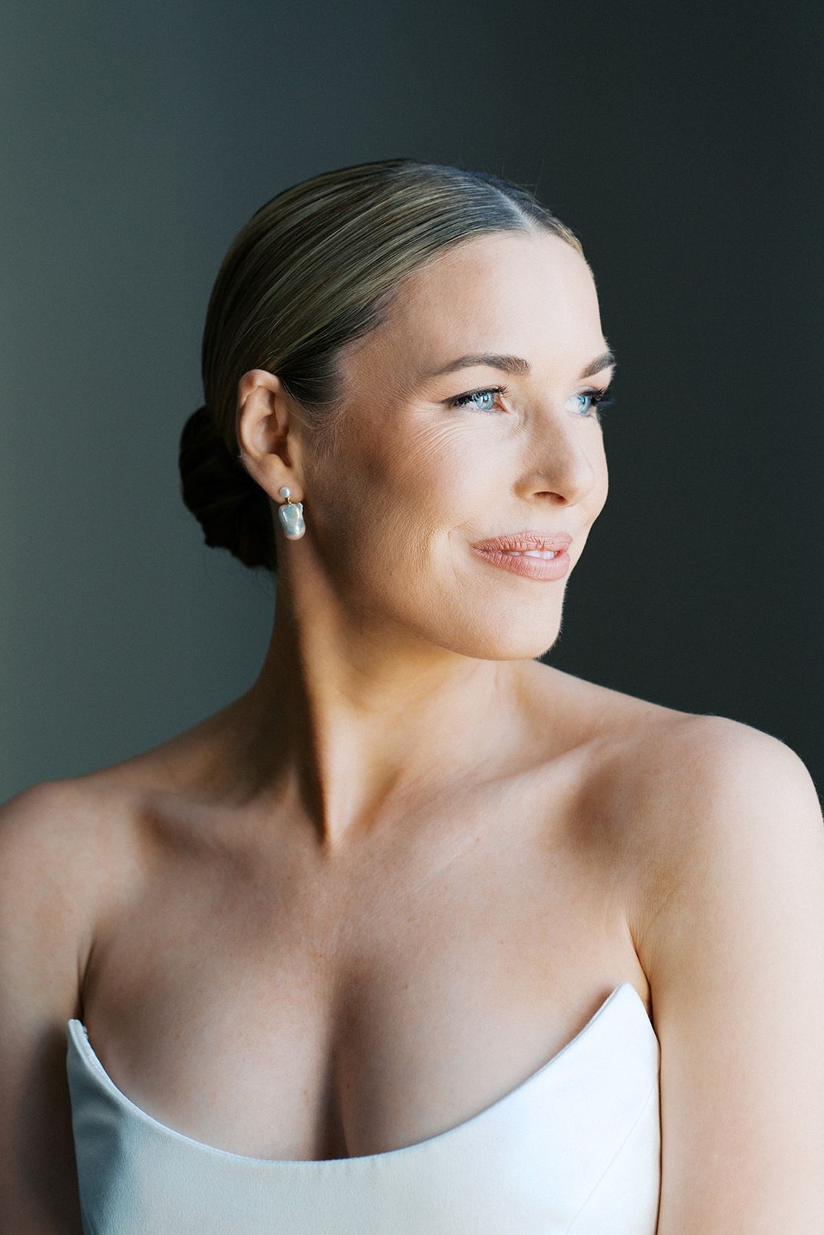 Bridal portrait of the bride with slick low bun, pearl earrings, and strapless ivory gown
