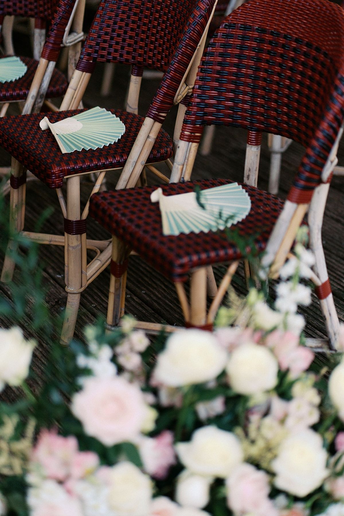Sage green paper hand fans on red Parisian bistro ceremony chairs with blush florals