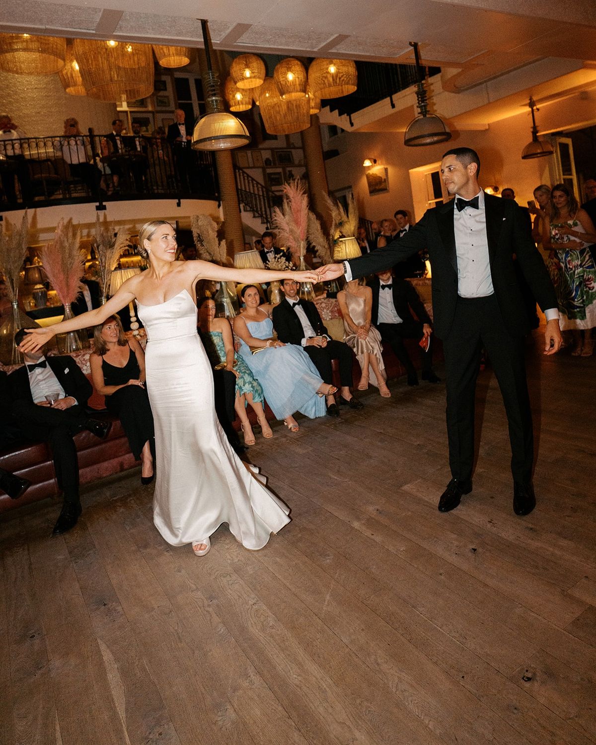 Couple's first dance under woven pendant lights with seated guests and pampas grass behind