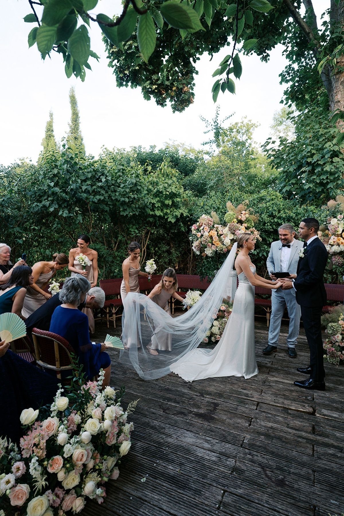 Couple holding hands at the floral altar with bridesmaids adjusting the bride's veil