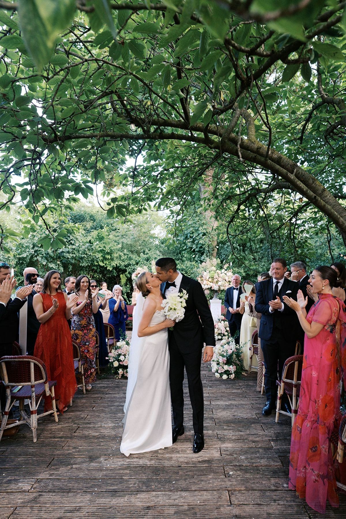 Couple's first kiss as a married couple beneath the leafy aisle as guests applaud