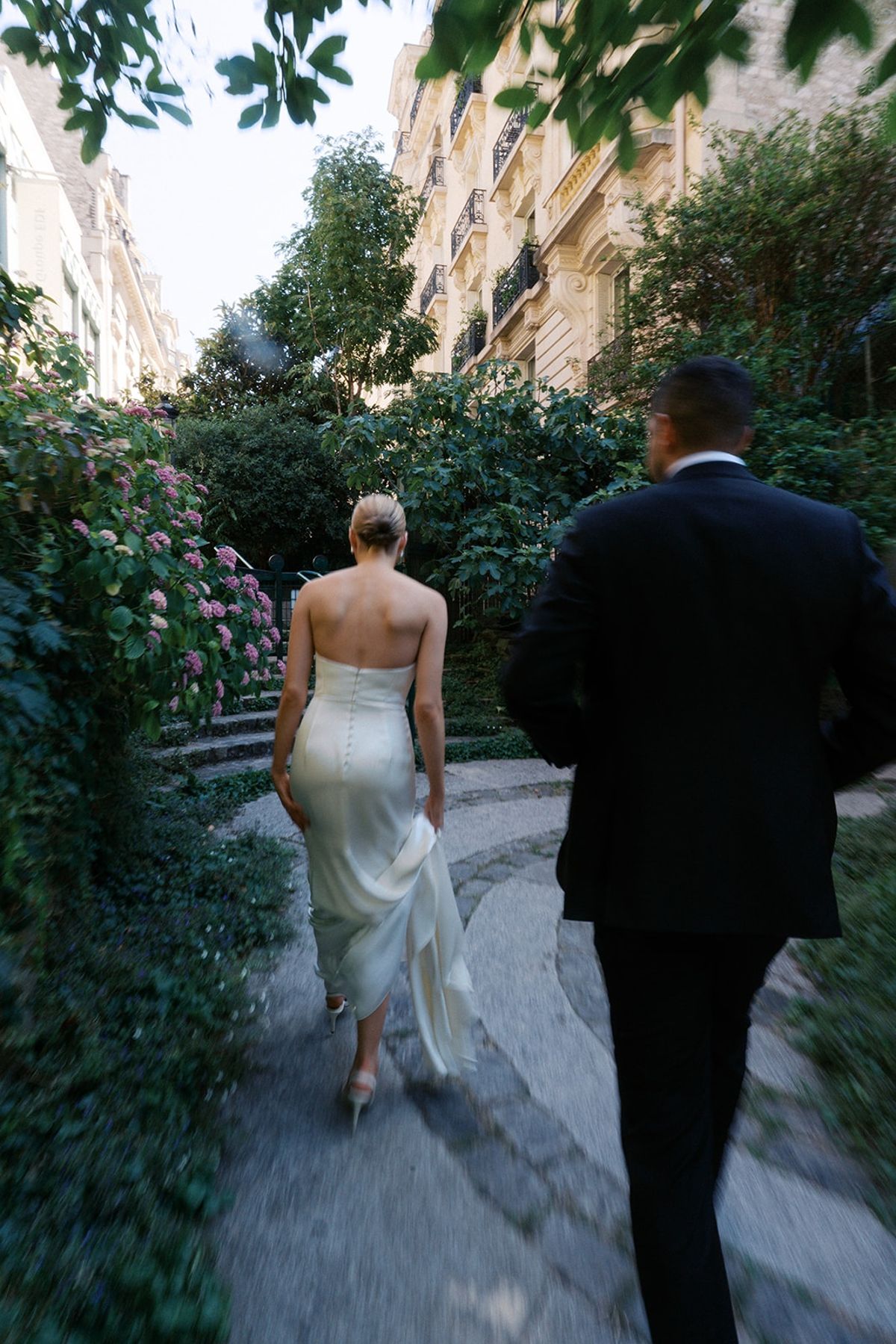 Couple walking away down a leafy Paris pathway beside flowering hydrangea
