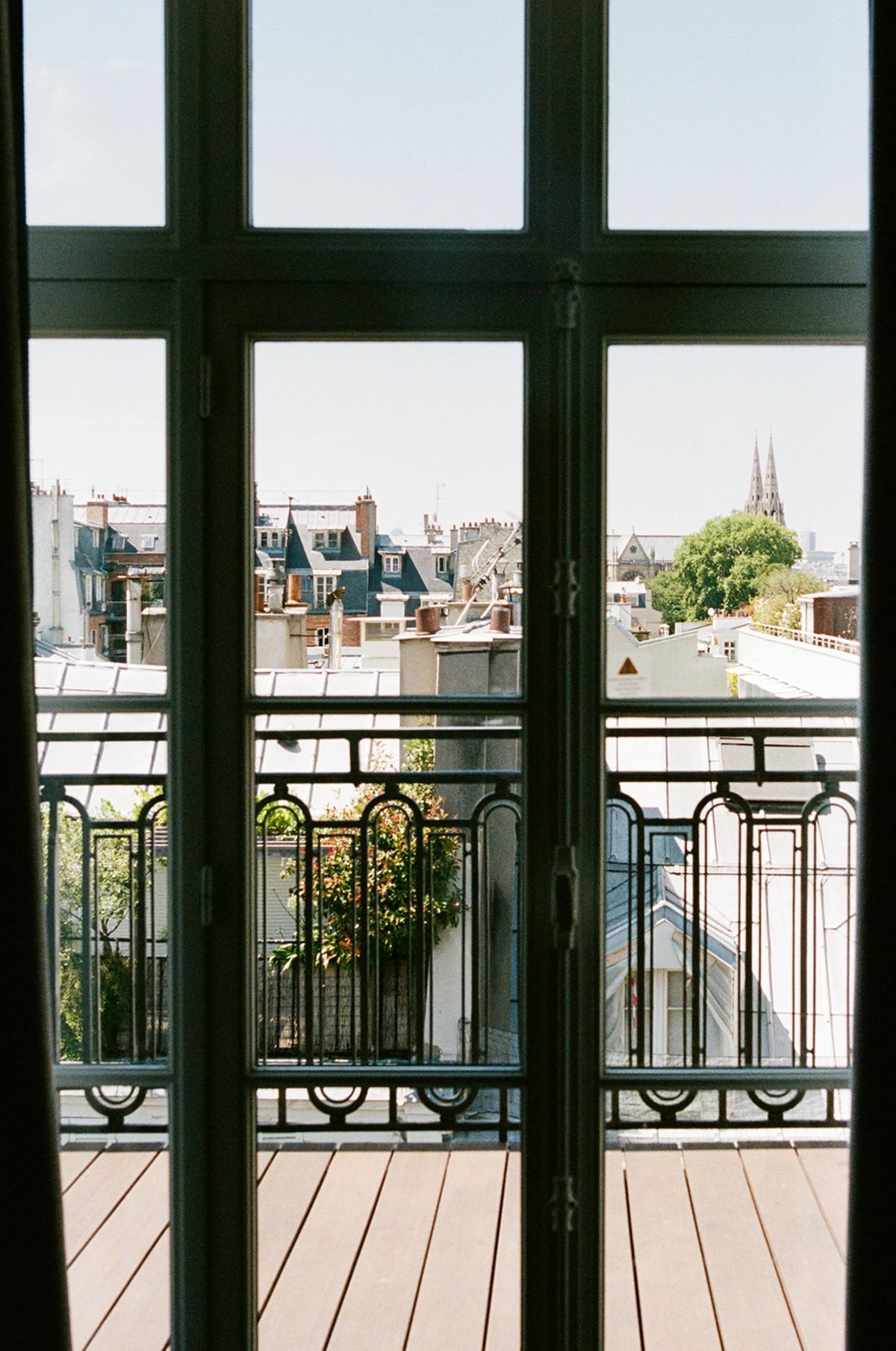 View through hotel French doors over Paris rooftops with a Gothic spire on the horizon