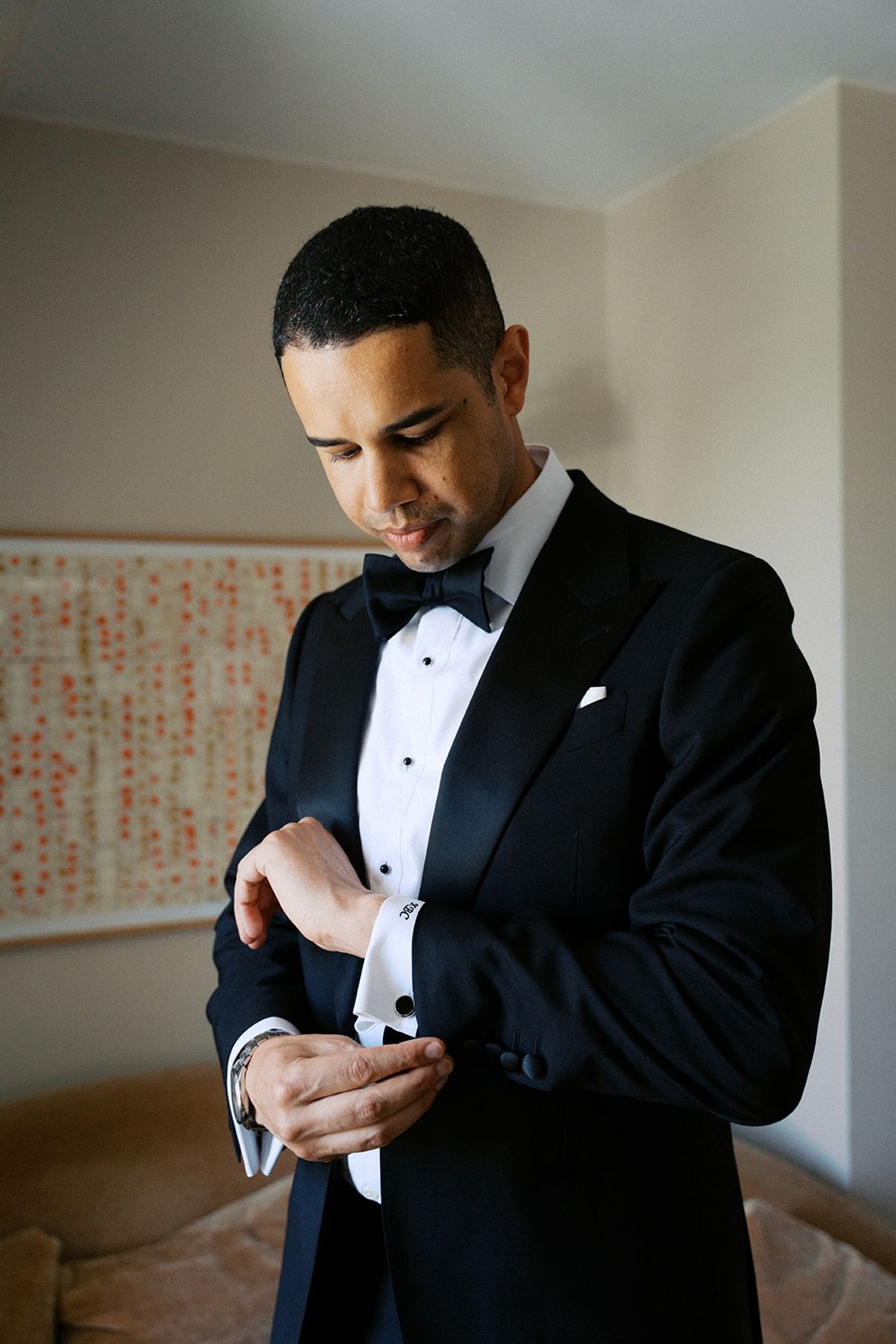 Groom adjusting his cufflinks in a black tuxedo and bow tie inside a Paris hotel suite
