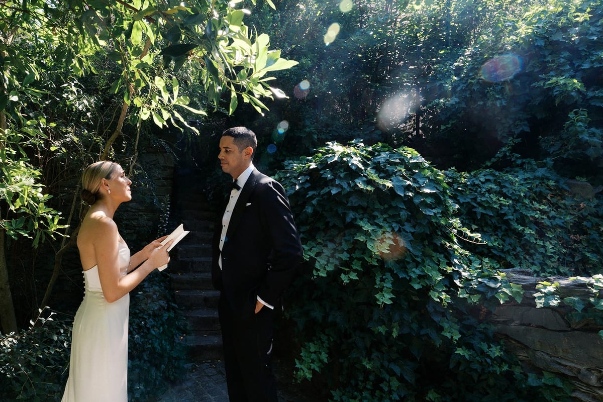 Bride reading her vows to the groom on a private garden staircase in dappled golden light