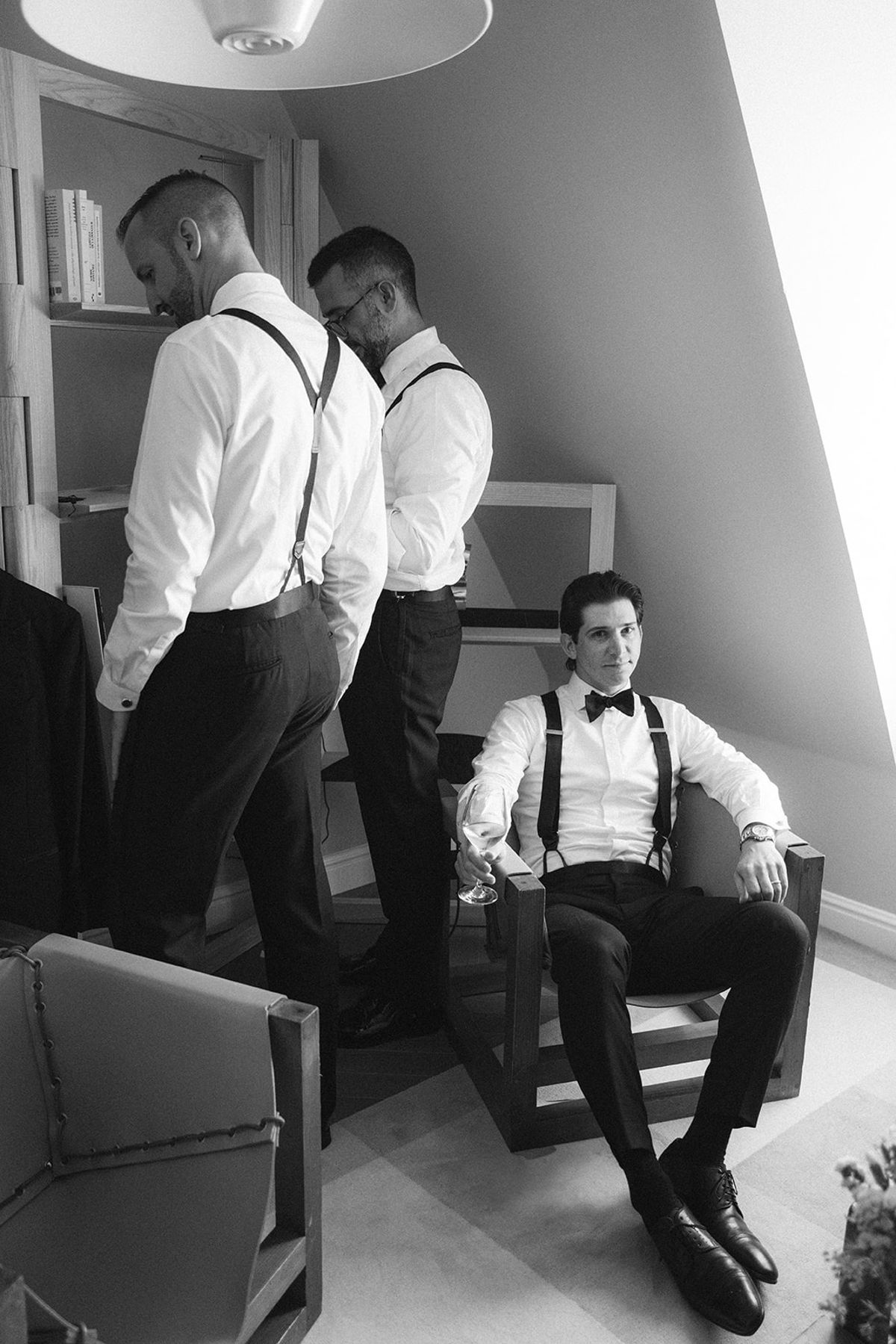 Black and white image of three groomsmen and the groom in white shirts and braces in a hotel attic