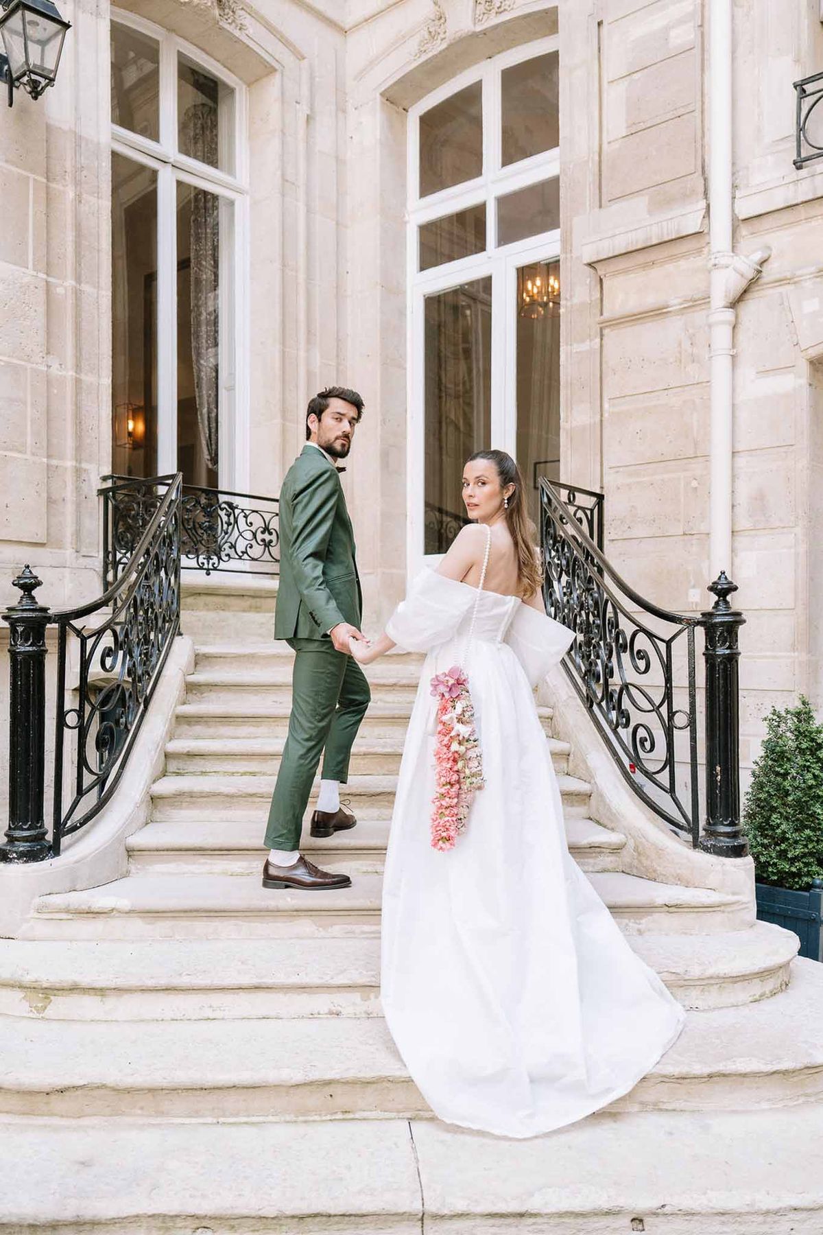 Couple on Haussmann staircase, groom in green suit, bride in ballgown with cascading blush hydrangea skirt