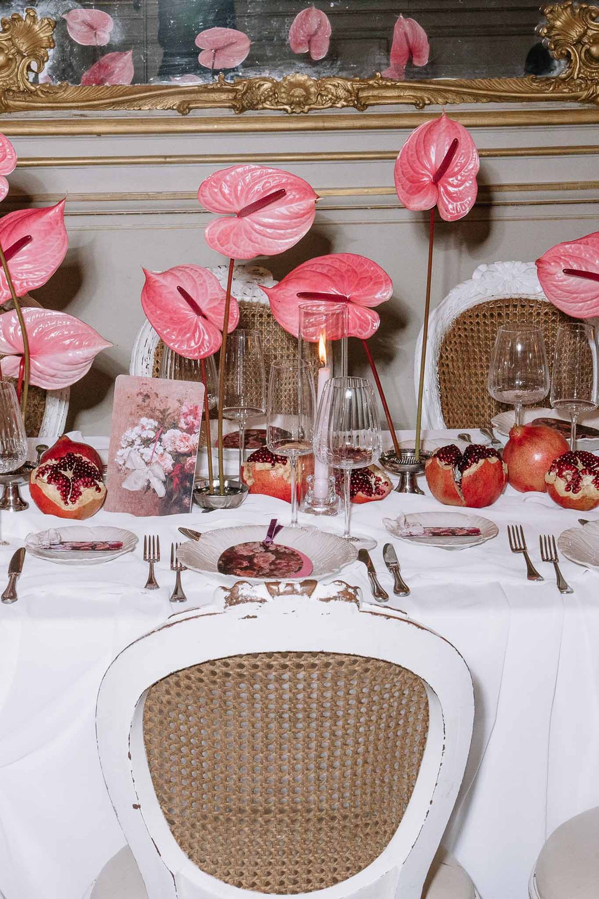 Reception table with pink anthurium stems, pomegranate accents, and floral art cards by gold mirror