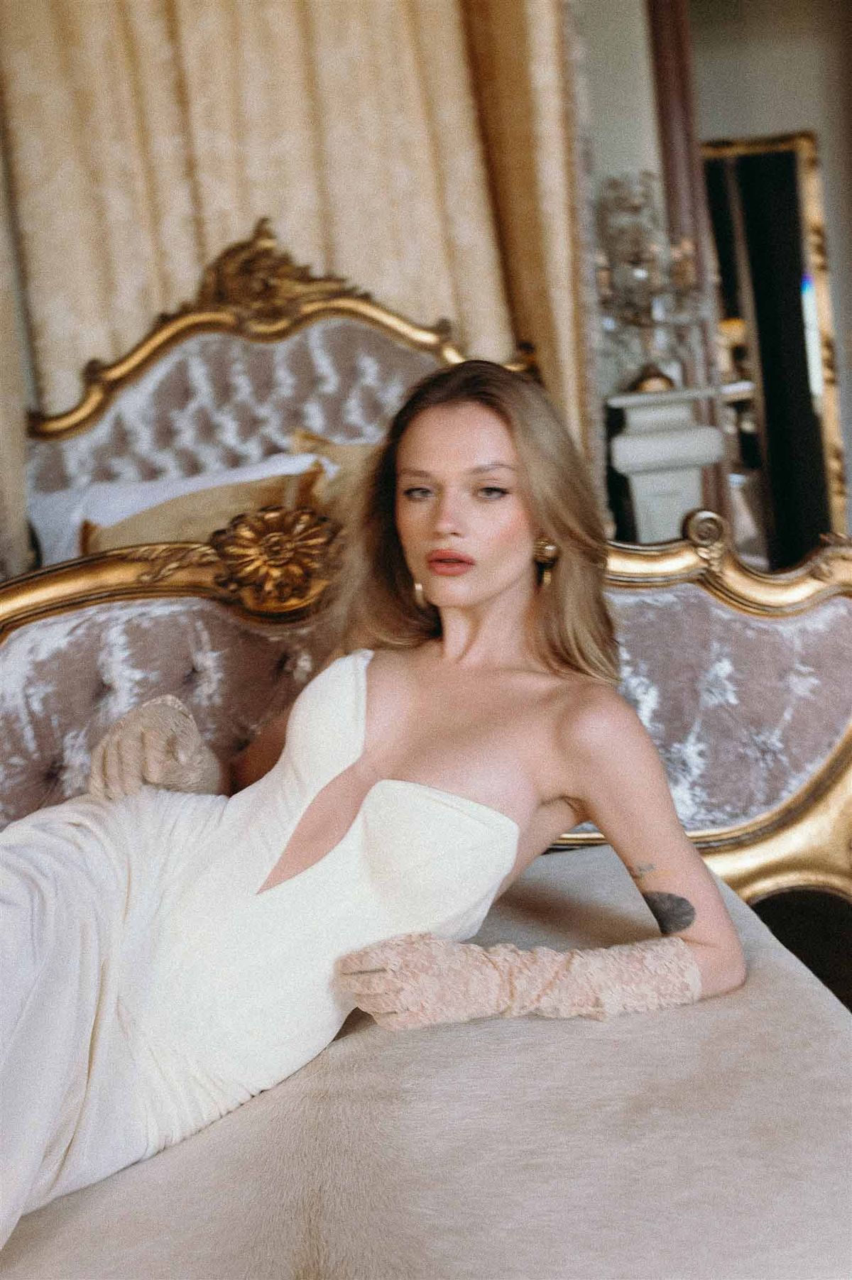 Bride in ivory strapless gown with blush lace opera gloves reclining on tufted velvet sofa in chateau