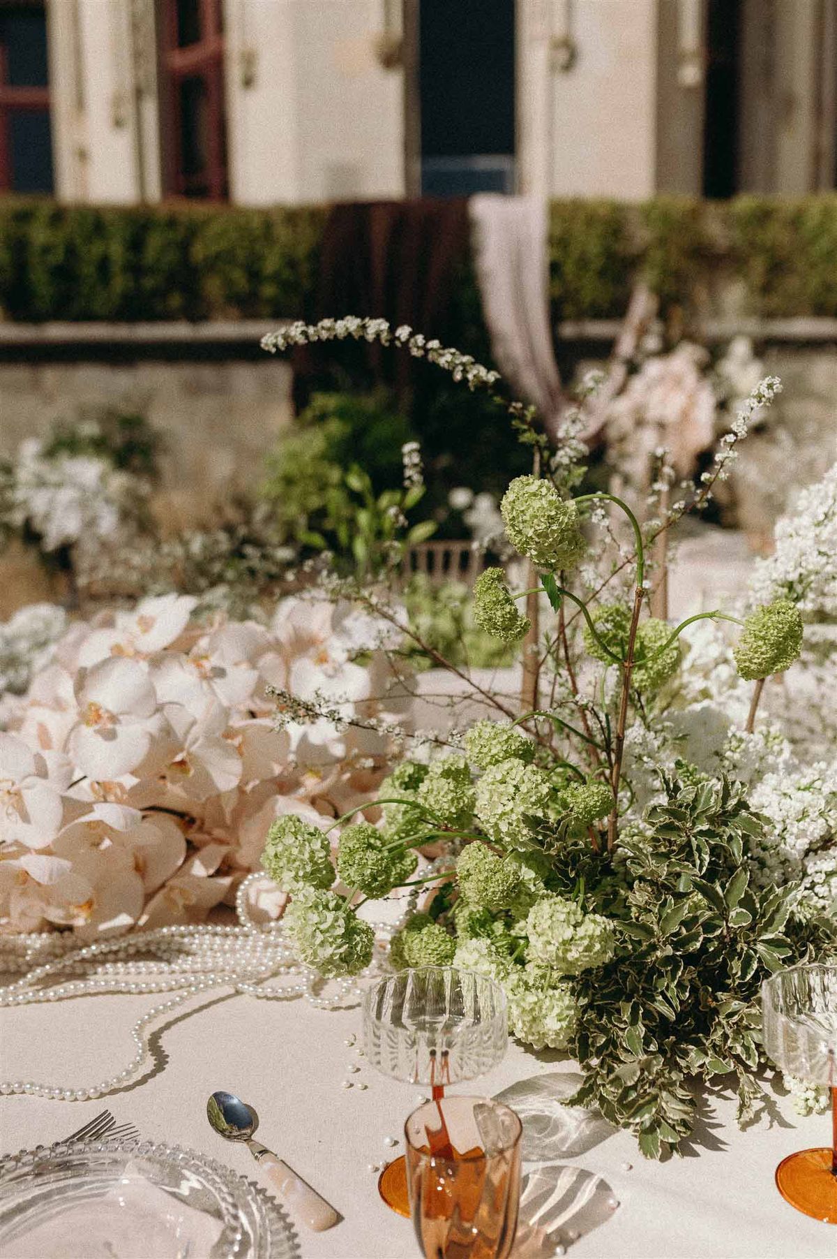 Centerpiece of blush orchids chartreuse viburnum and spirea with pearl strands and amber glassware