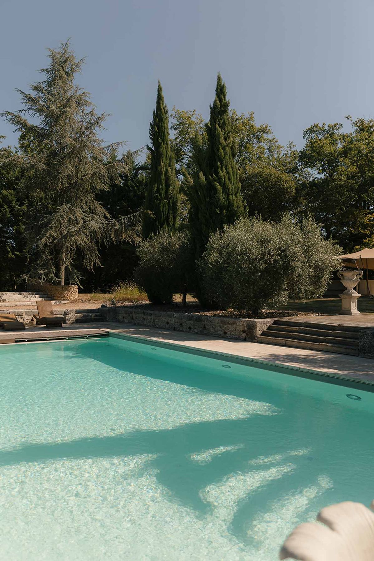 Rectangular turquoise pool with stone terrace, retaining walls, and classical urn planter at country estate