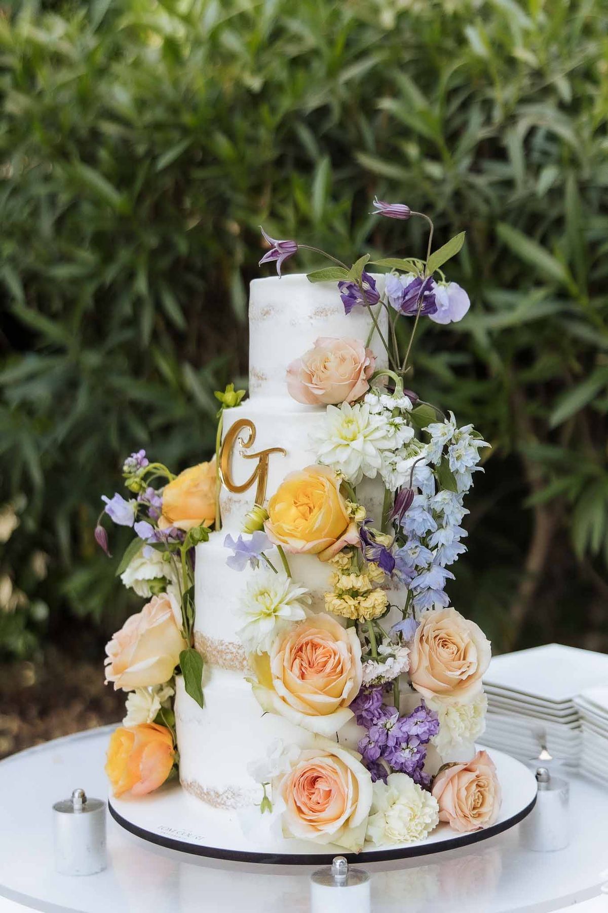 Four-tier marble-effect cake with gold monogram and cascading peach roses and blue delphinium