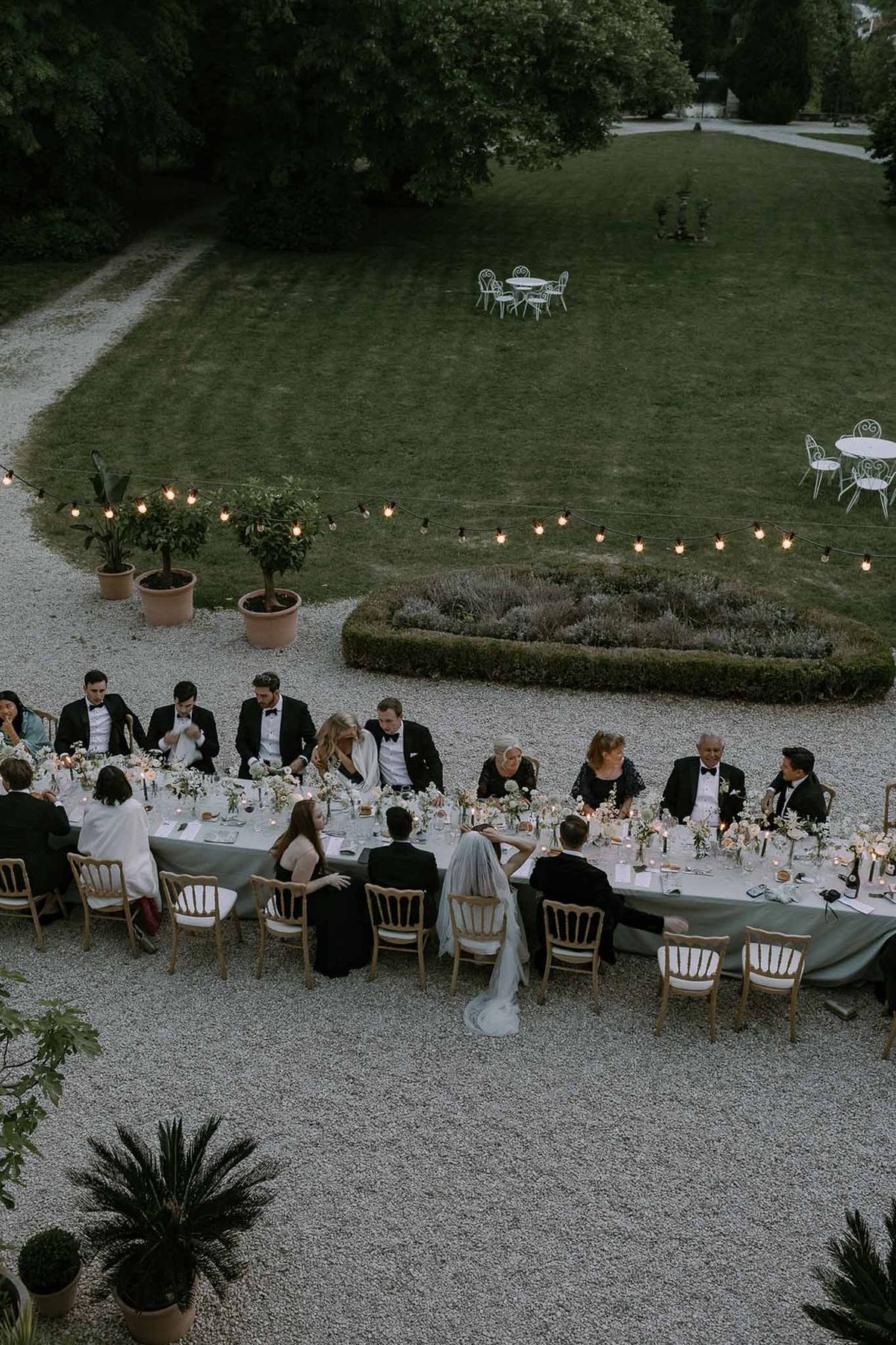 Aerial dusk reception with bride and groom at sage-linen banquet table with Edison string lights