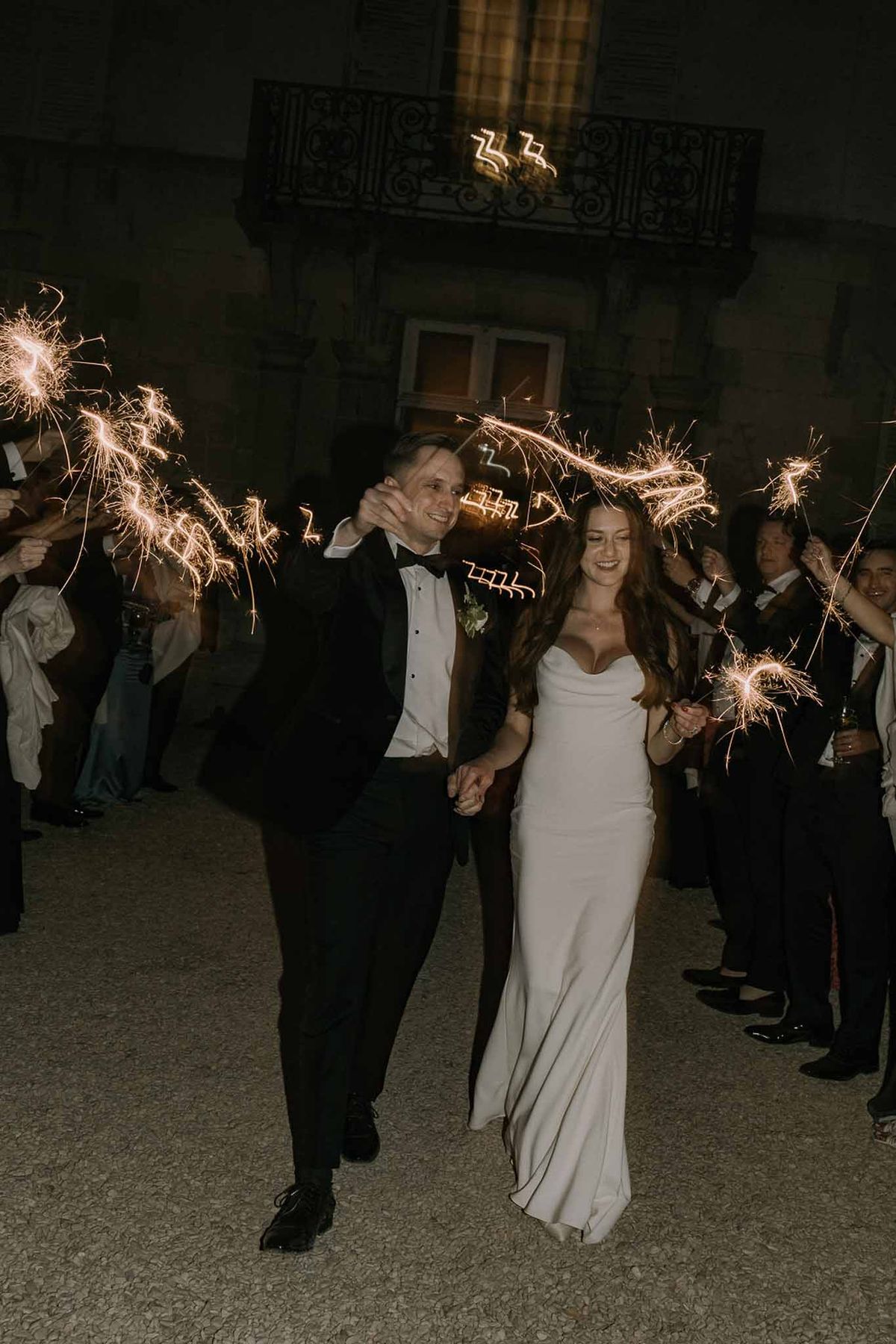 Bride and groom sparkler exit at night walking through guest tunnel at a French chateau courtyard