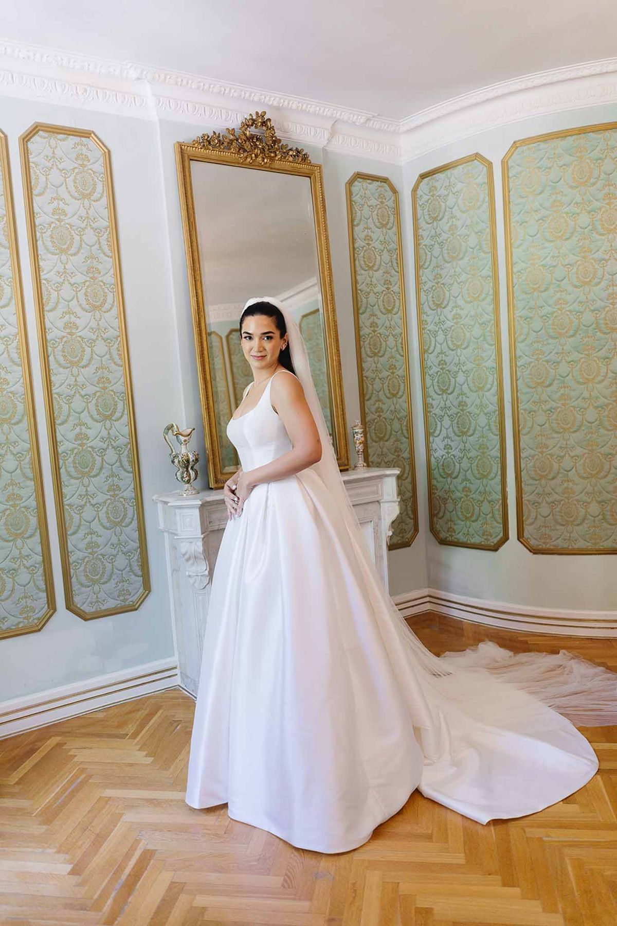 Bride in white satin ball gown with cathedral train and veil in ornate French room with gilt mirror