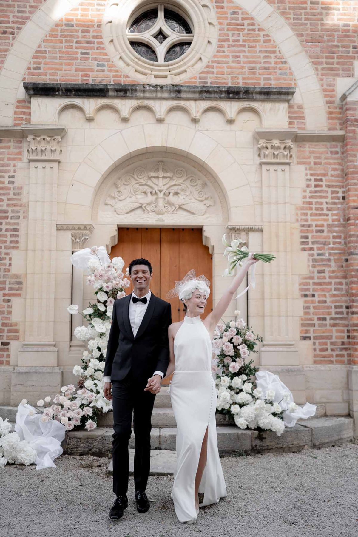 Couple exiting brick chapel with calla lily bouquet raised past white hydrangea staircase arrangements