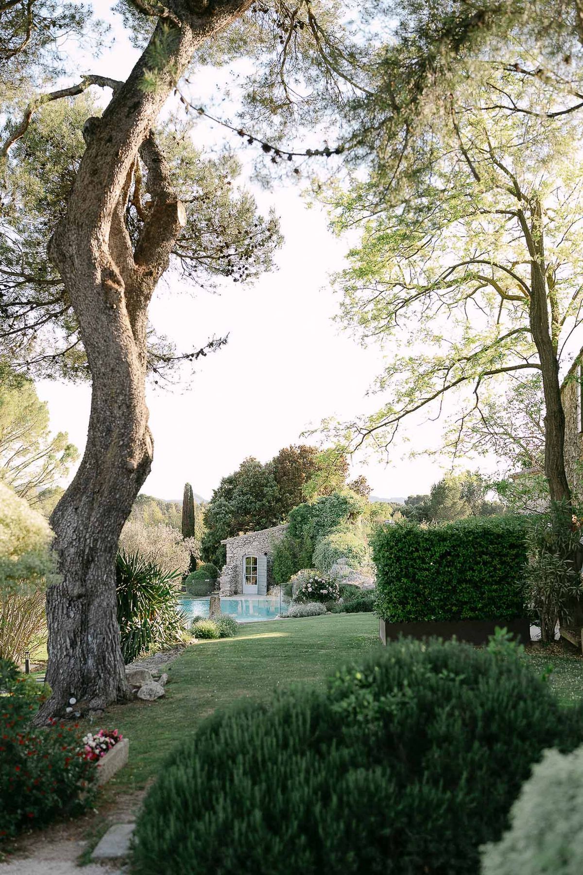 French estate grounds with pool, stone outbuilding, box hedging, bistro lights, and cypress tree