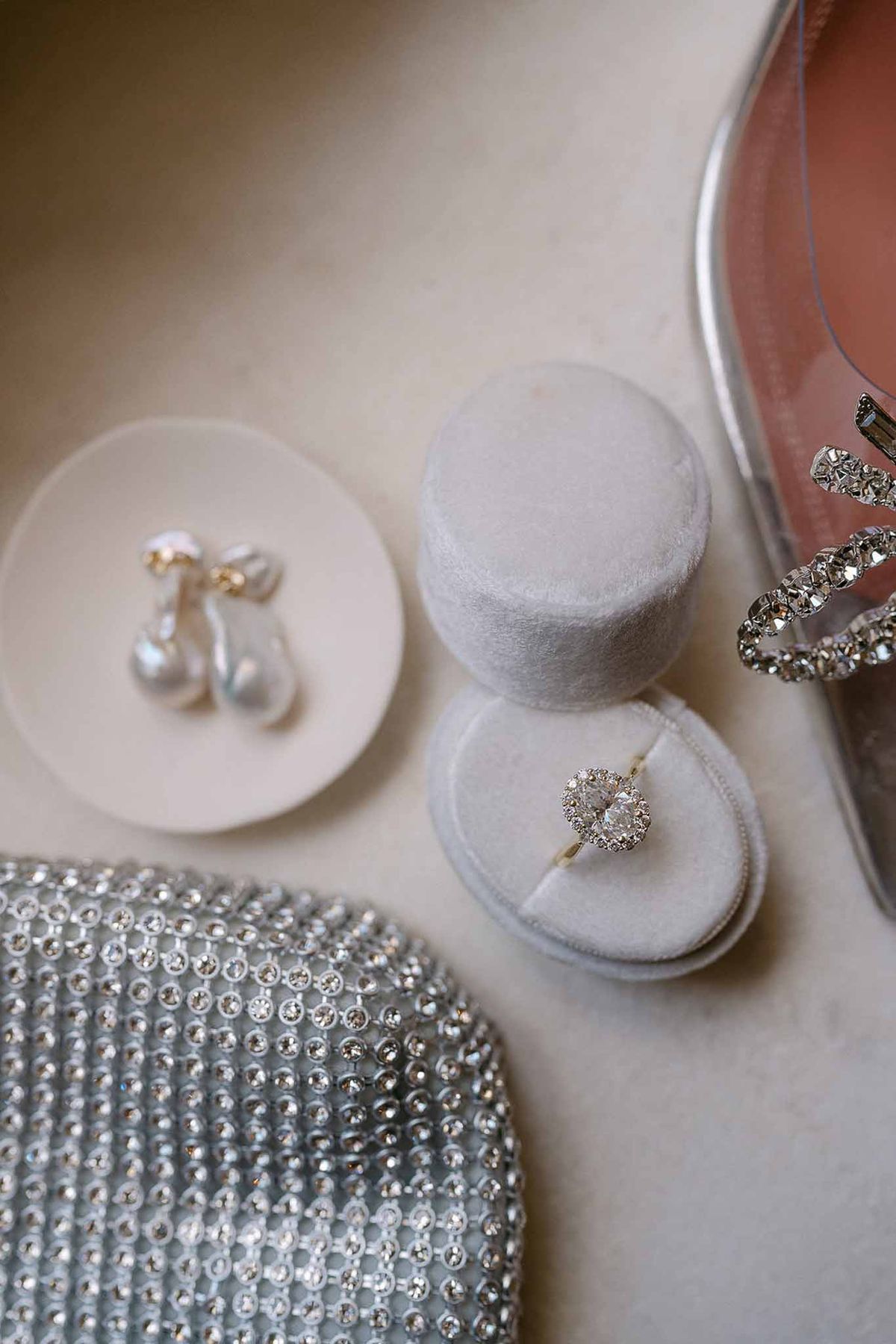 Pear-cut diamond ring in grey velvet box with baroque pearl earrings and crystal clutch on cream surface