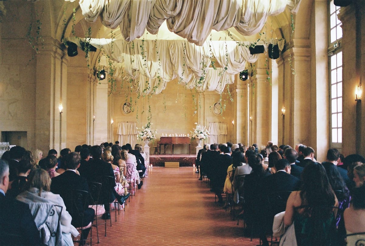Analog wide of ceremony hall with guests in iron chairs beneath draped fabric canopy