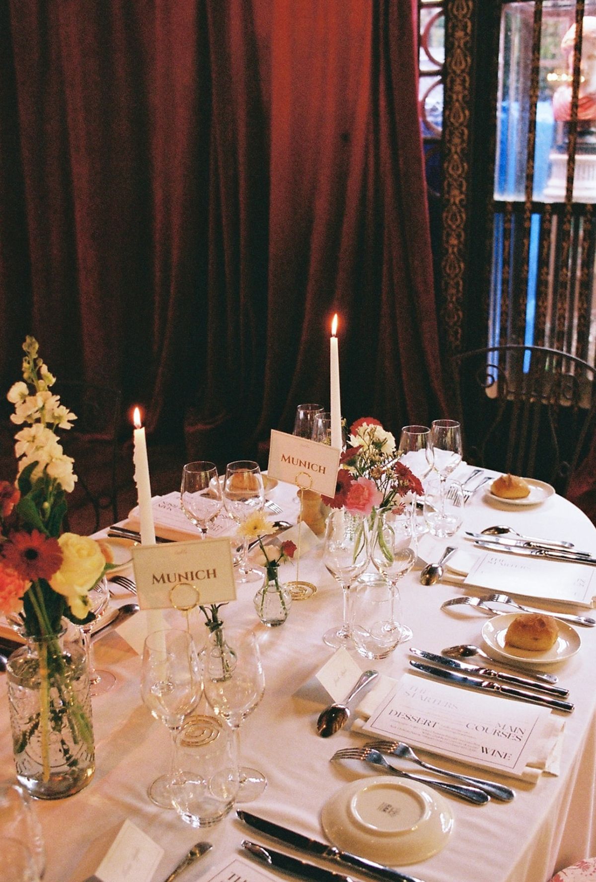 Analog detail of candlelit dinner table with pastel blooms, Munich cards and tapers