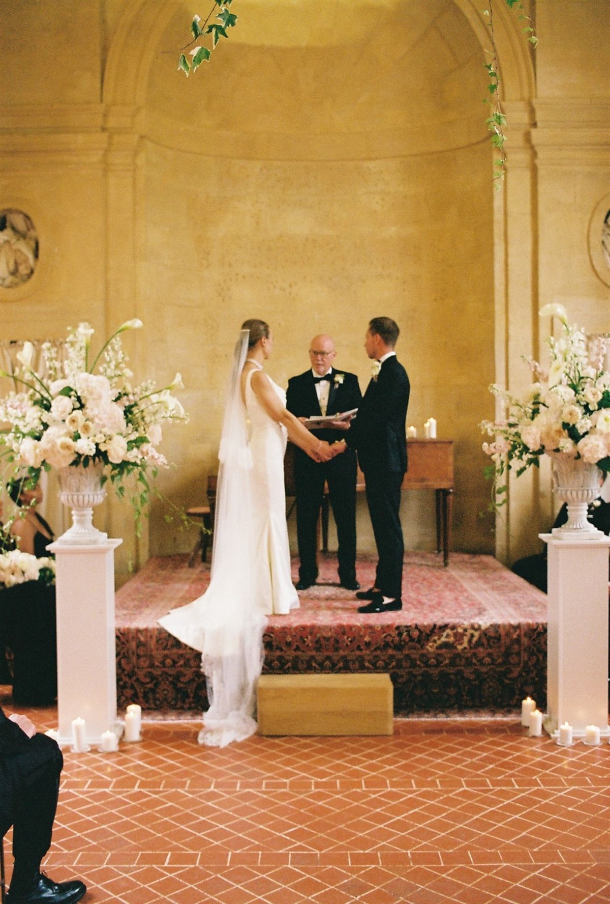 Couple holds hands at altar before officiant between blush and white floral urns