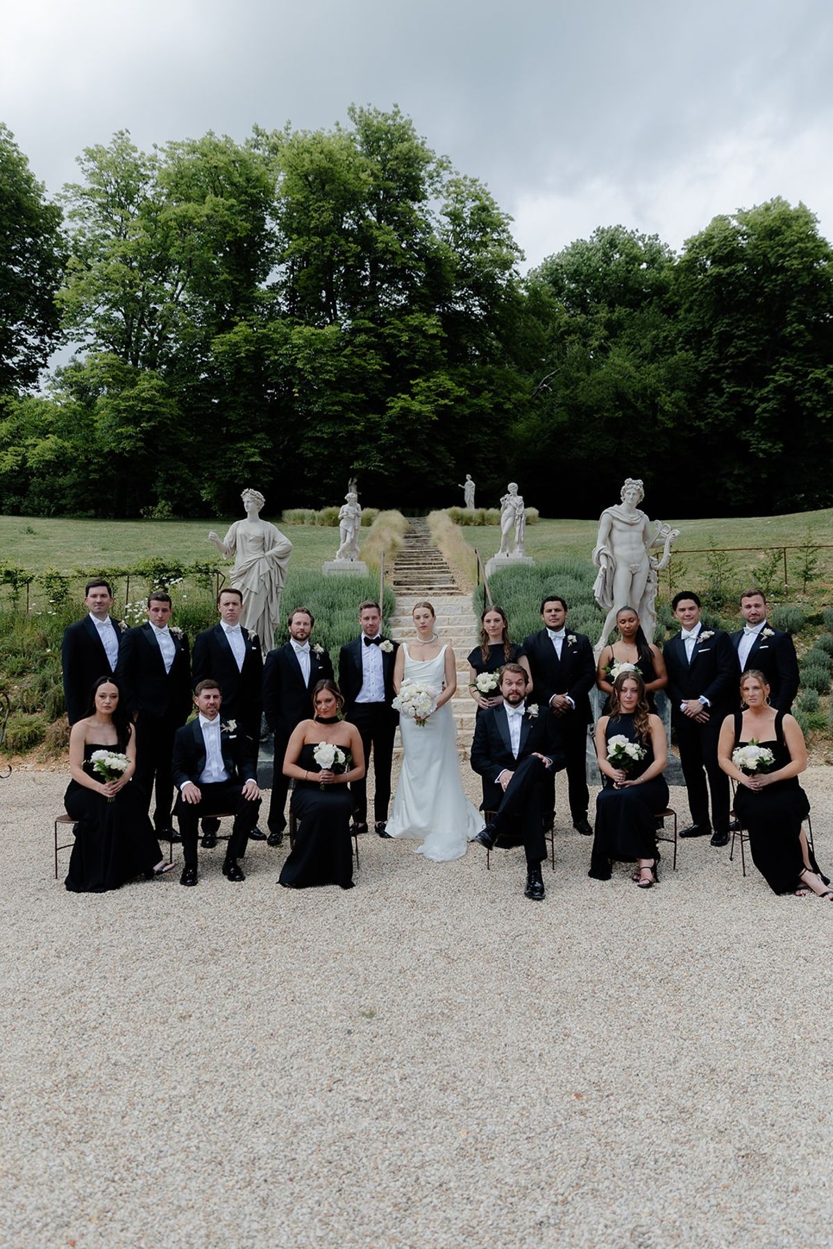Bridal party around bride and groom in formal lavender allee with classical statues