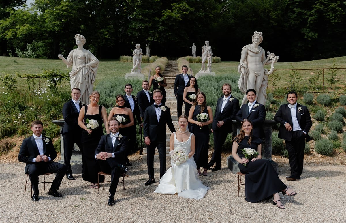 Bridal party portrait with bride and groom seated centre under lavender staircase