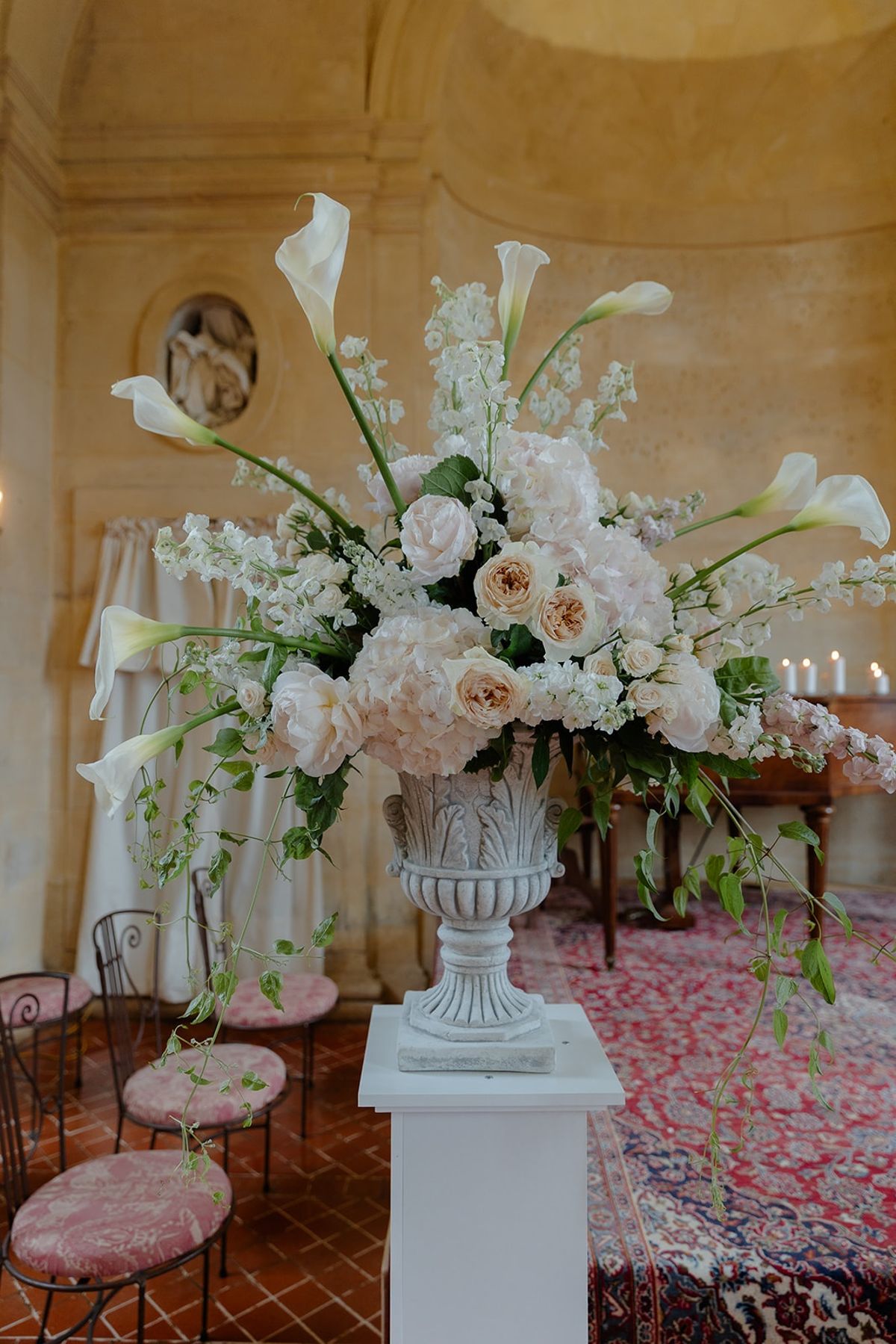 Blush and ivory floral urn arrangement of roses and calla lilies on white plinth