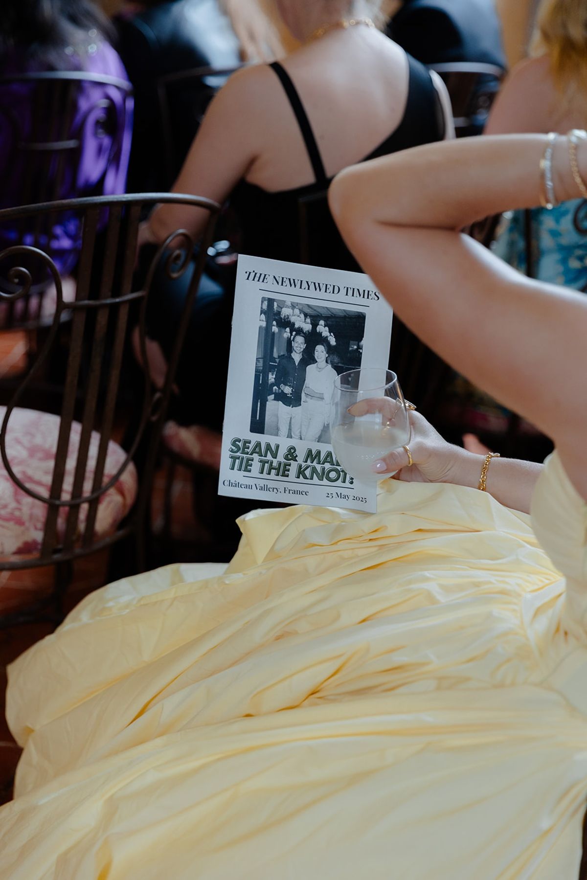 Guest in yellow gown holds newspaper-style wedding program on her lap
