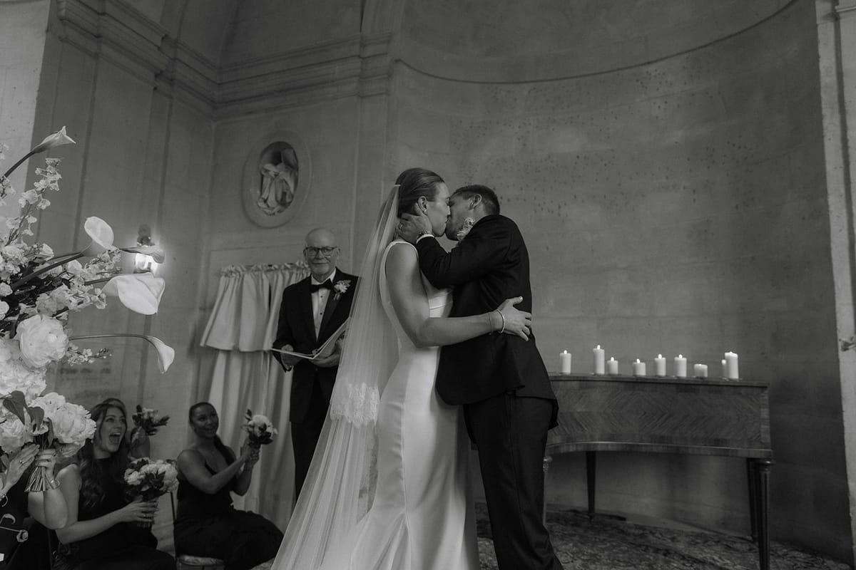 Couple shares first kiss as married pair before officiant with guests applauding