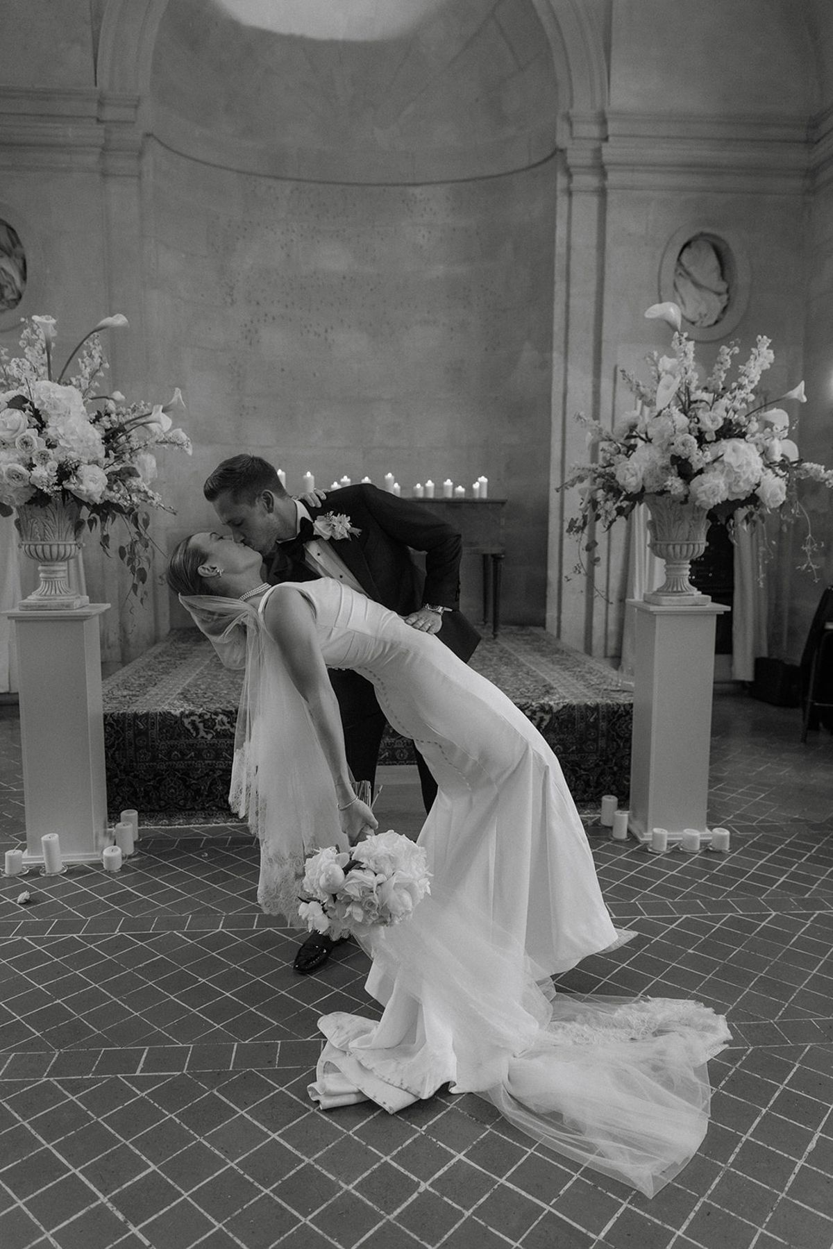 Groom dips bride into a kiss at altar between blush and white floral urns