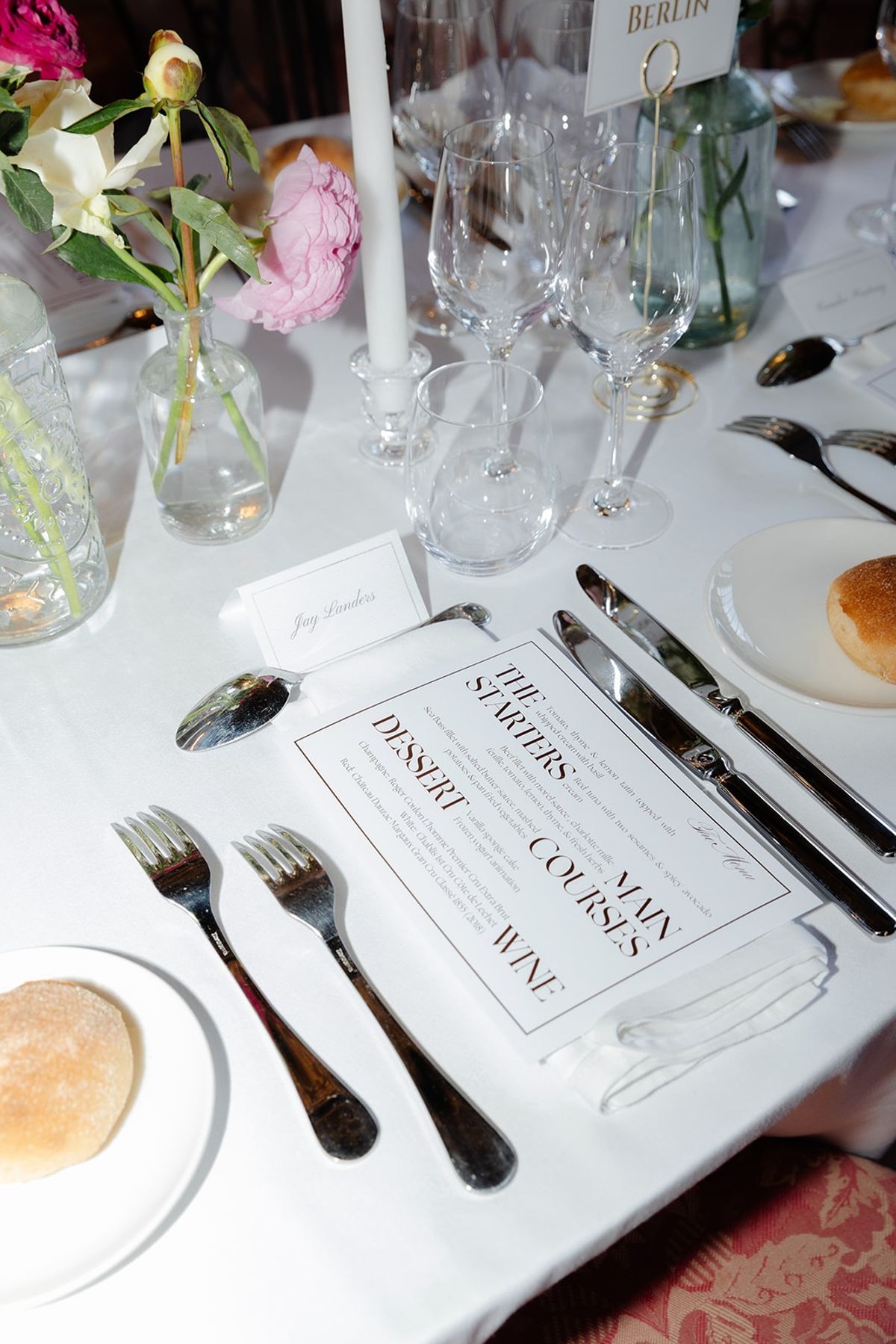 Place setting with crystal glassware, taper candle, peonies and bespoke menu card