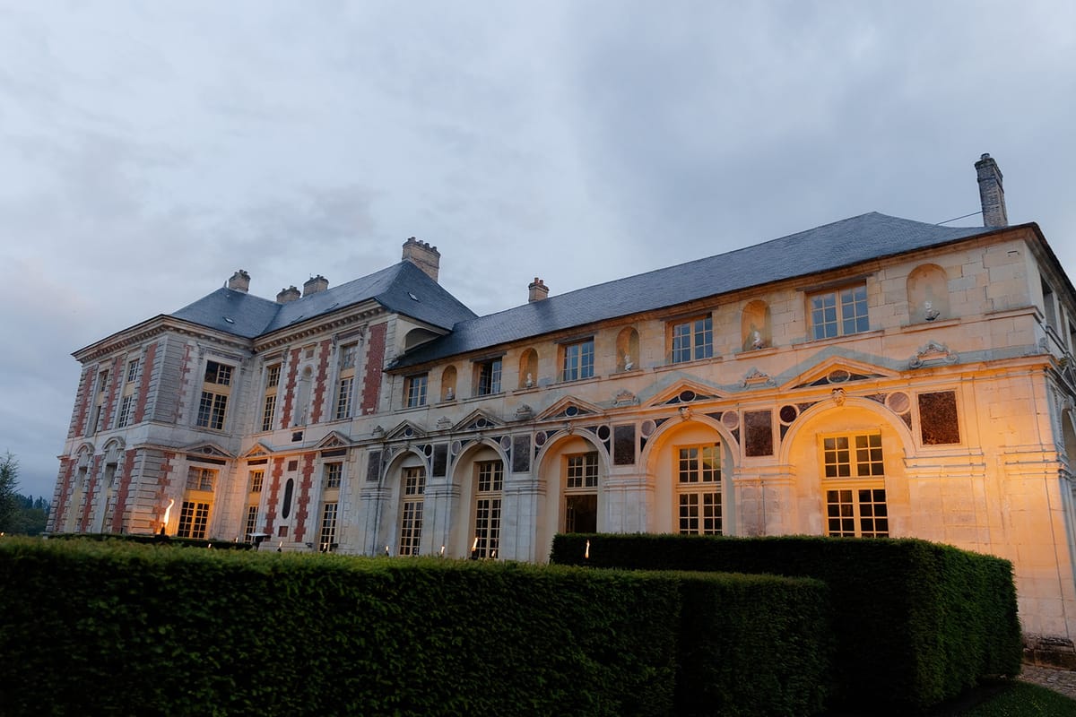 Grand chateau facade glows at dusk above a clipped hedge with arcaded ground floor