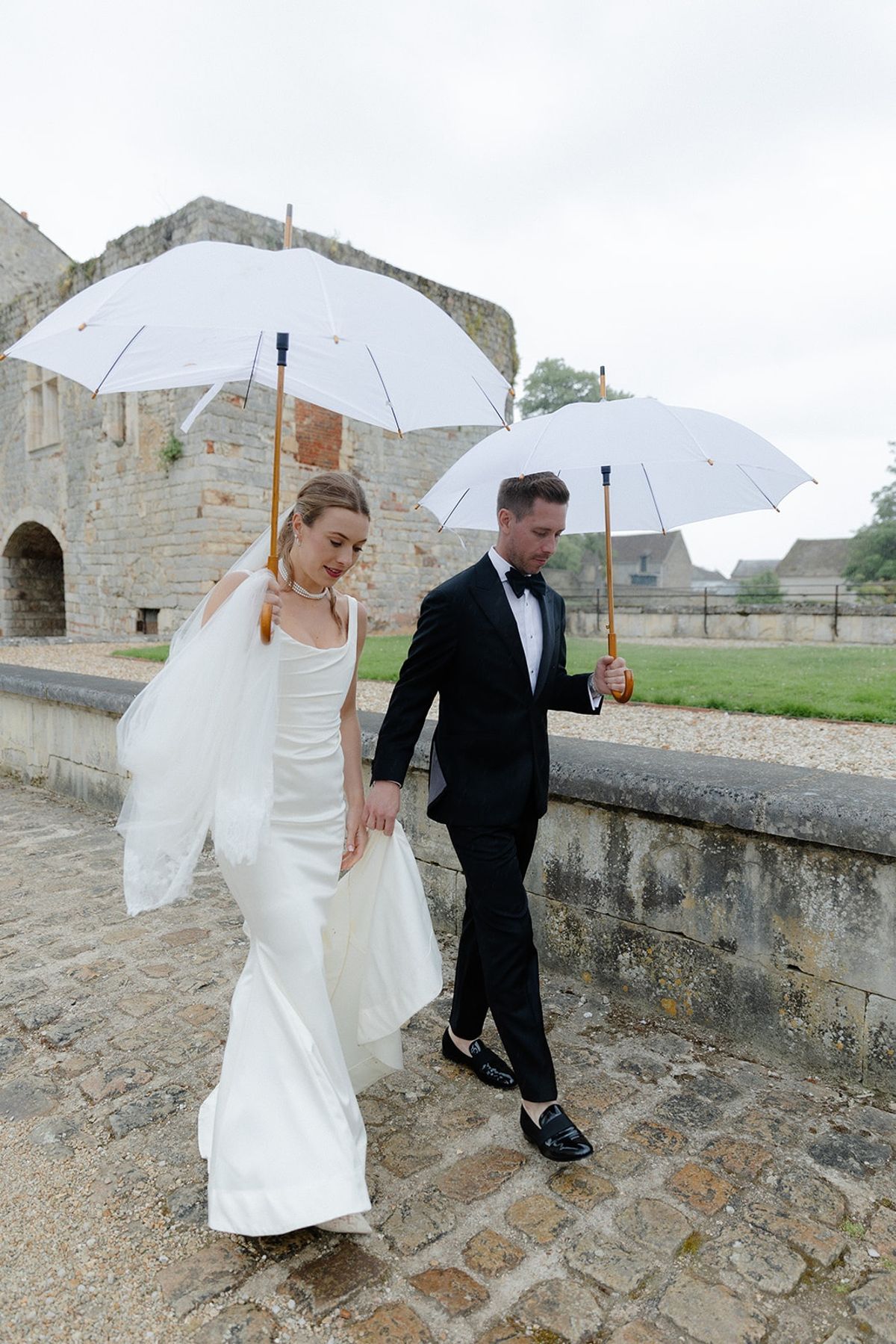 Couple walks under white parasols along cobbled chateau bridge