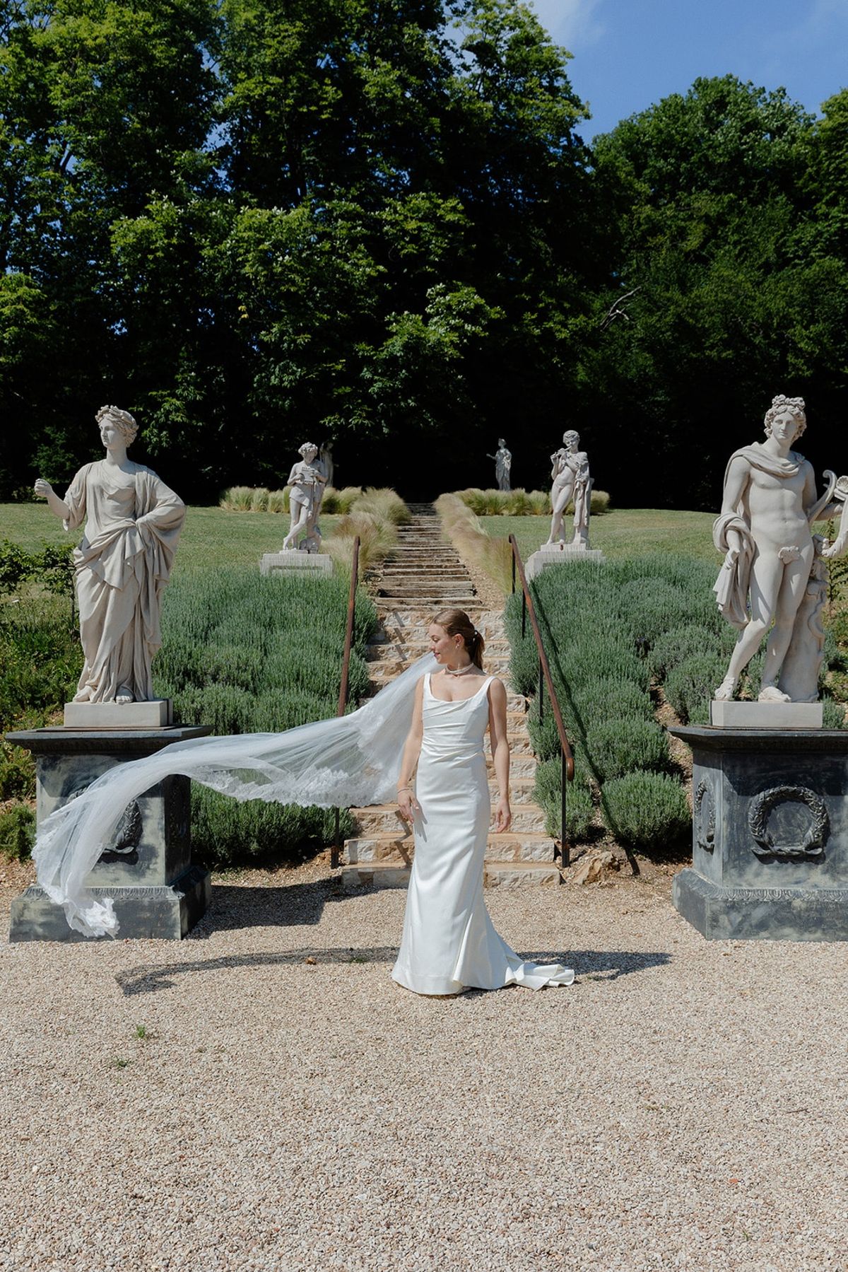 Bride stands at foot of long lavender allee flanked by classical statues