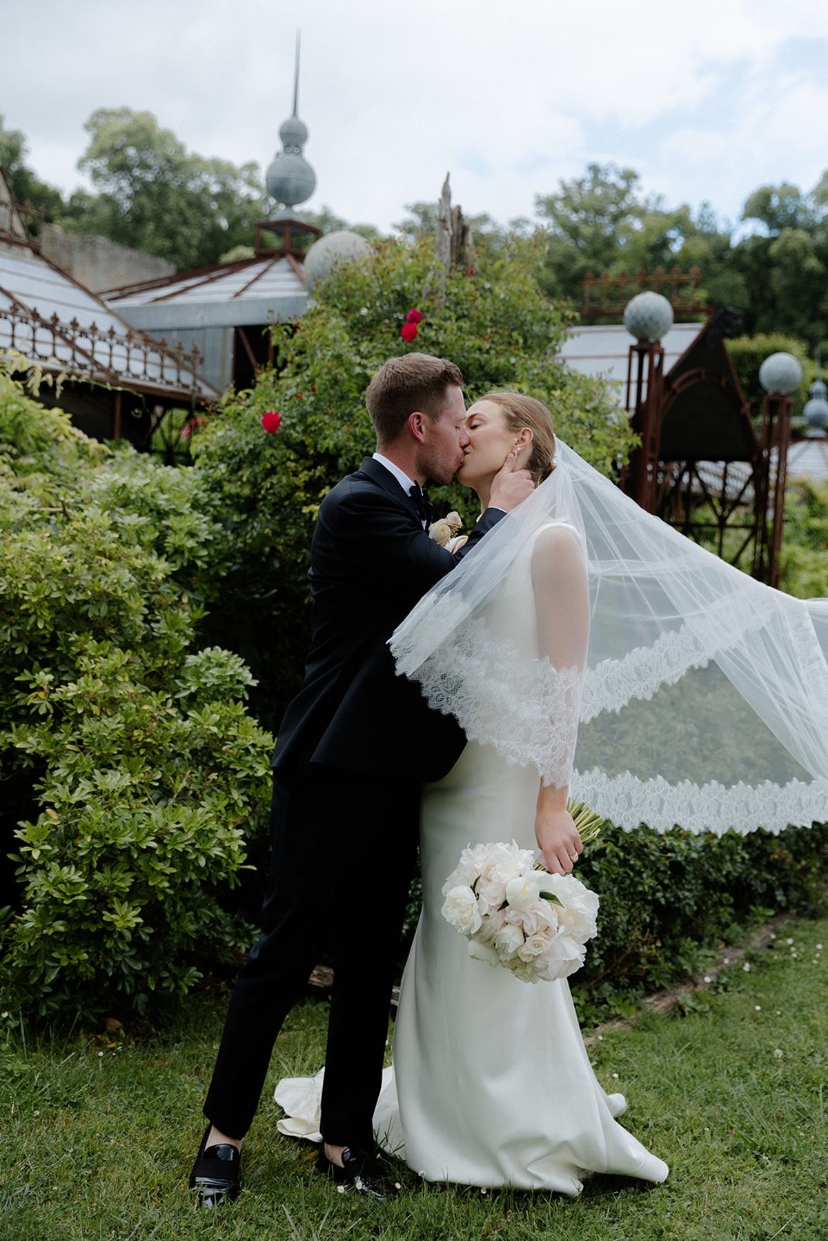 Bride and groom kiss in chateau kitchen garden with veil sweeping around them