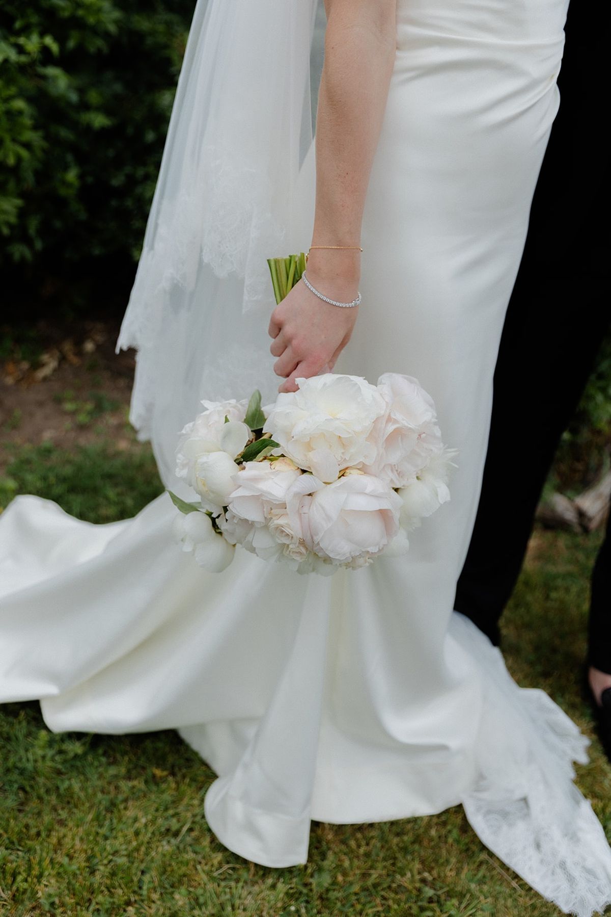 Close detail of bride's hand around white and blush peony bouquet with tennis bracelet