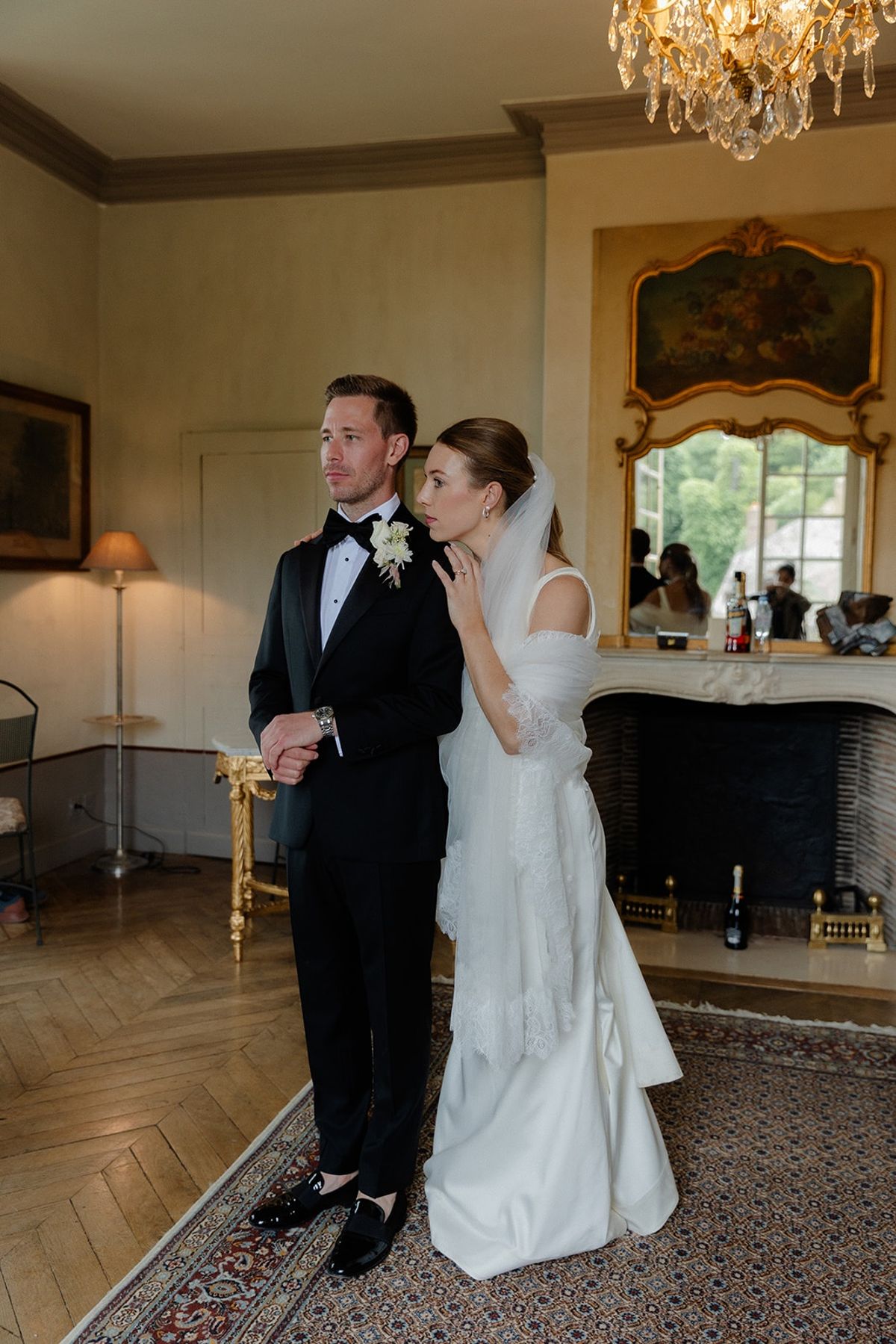 Bride leans into groom in antique chateau salon under crystal chandelier
