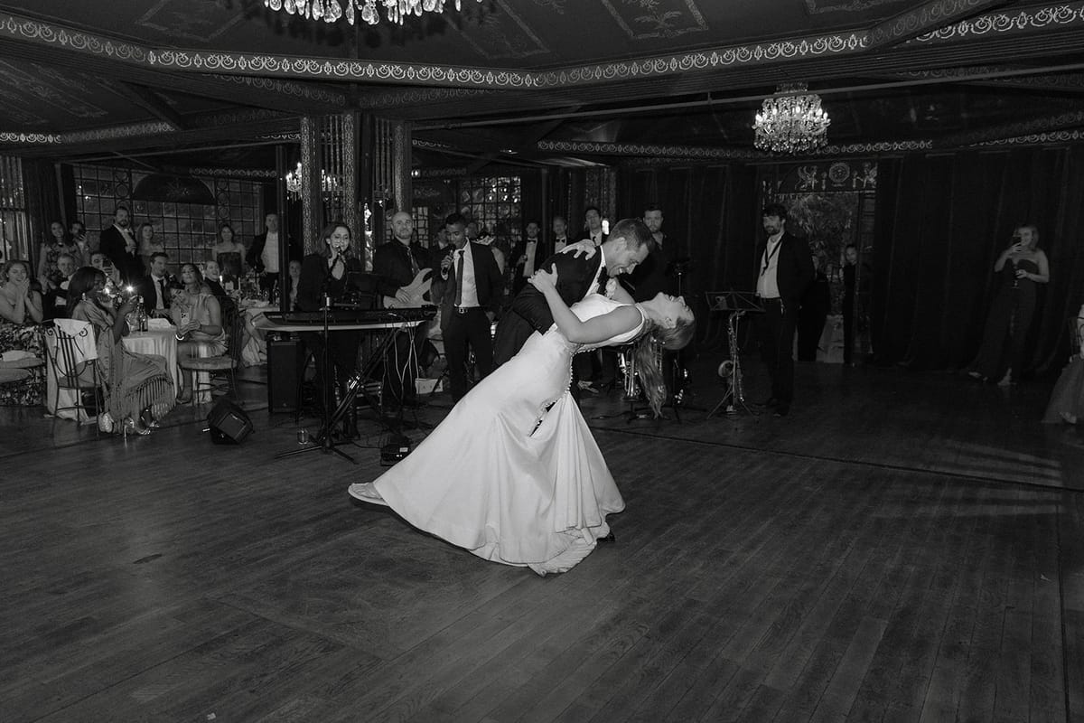 Bride and groom share first dance in chandelier-lit hall as groom dips the bride