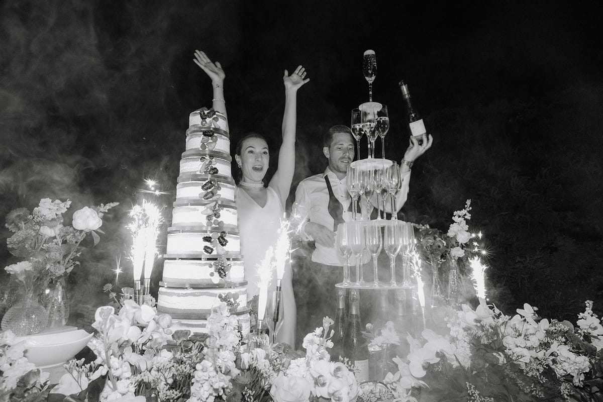 Couple cheers before six-tier fig wedding cake with champagne tower and sparklers